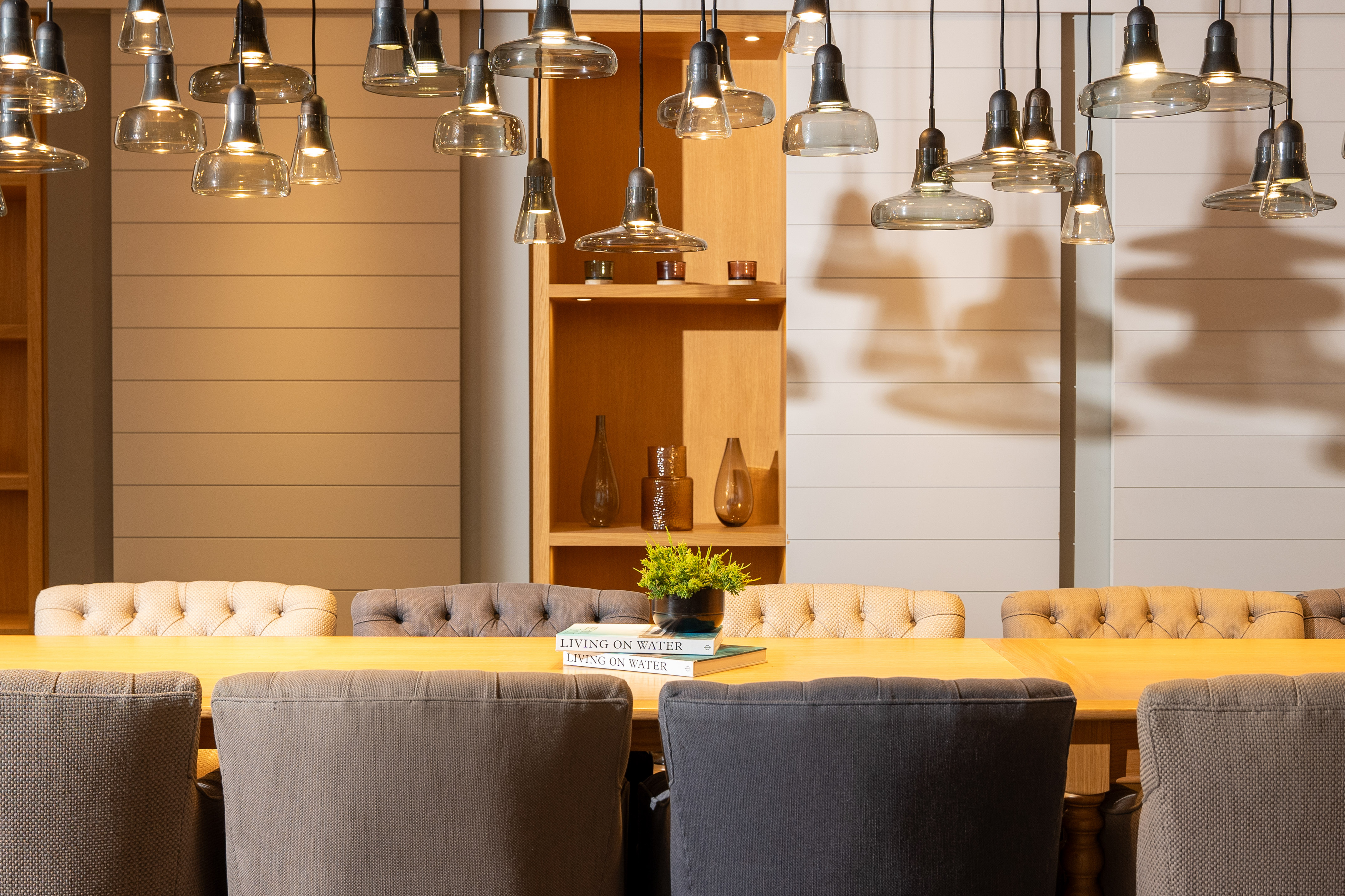 Contemporary dining room with glass pendant lights, wooden table, and tufted chairs.
