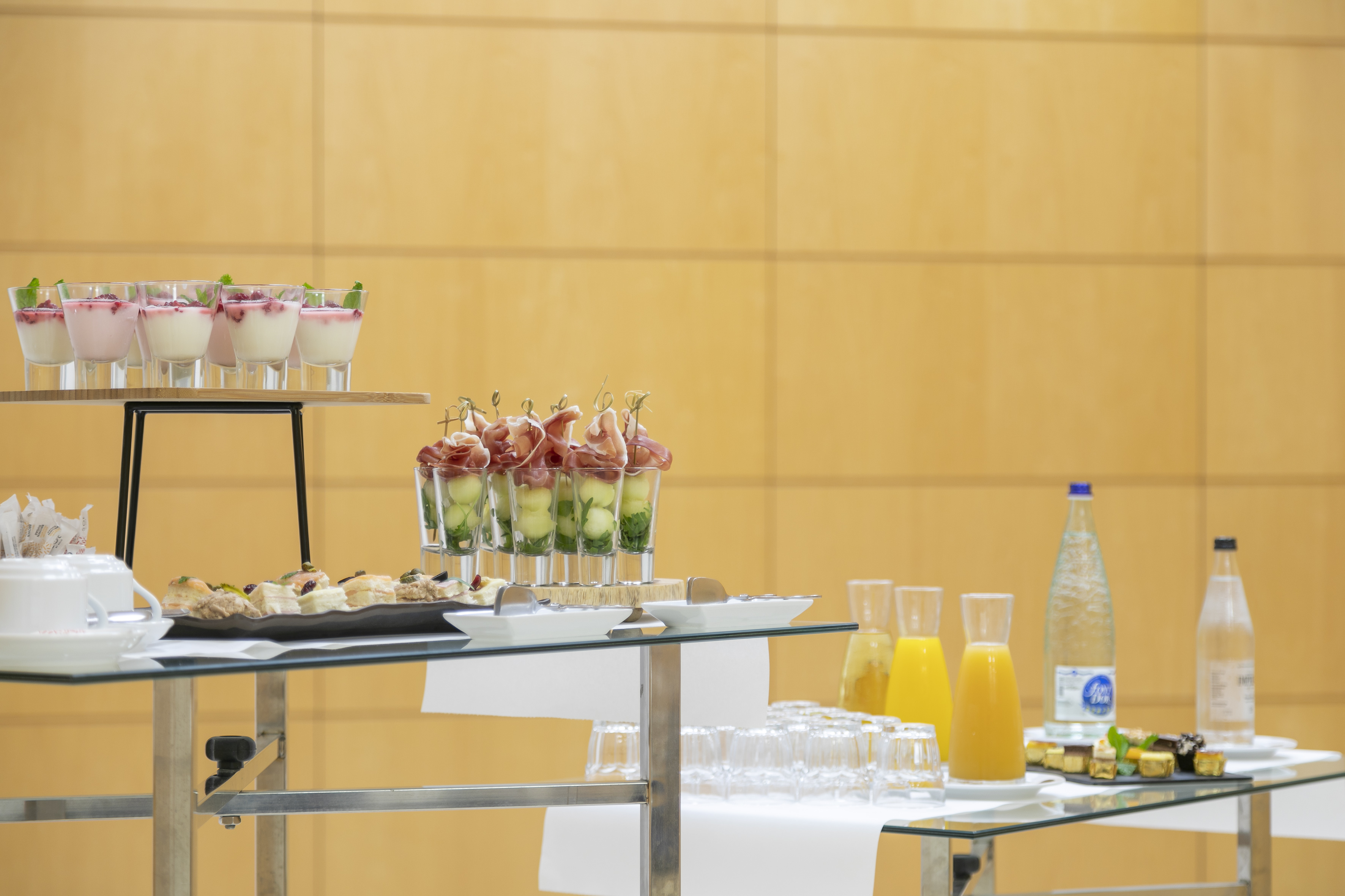 Catering buffet with panna cotta, canapés, prosciutto skewers, and drinks.