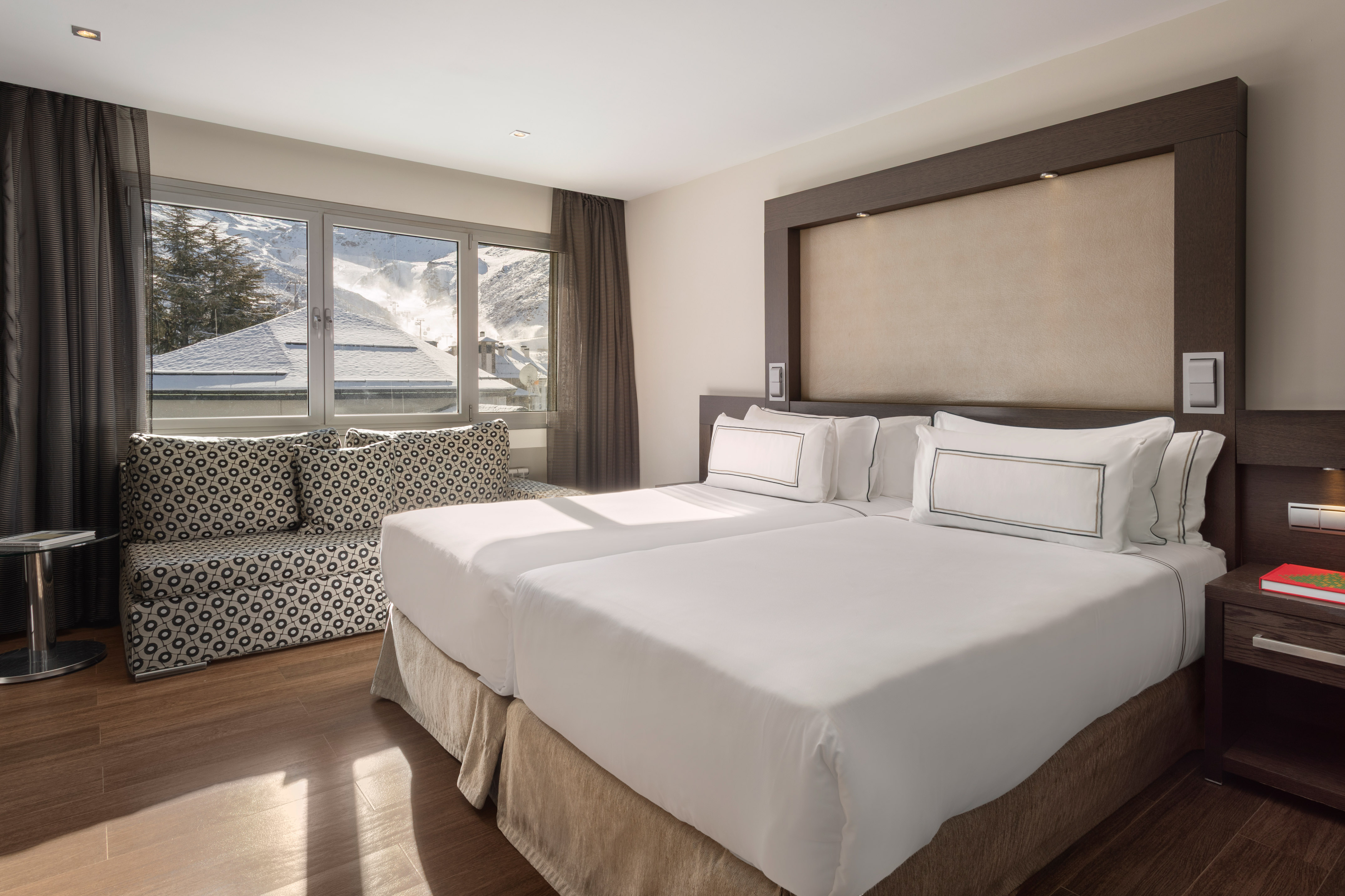 Modern hotel room with twin beds, sofa, and snowy ski resort view.