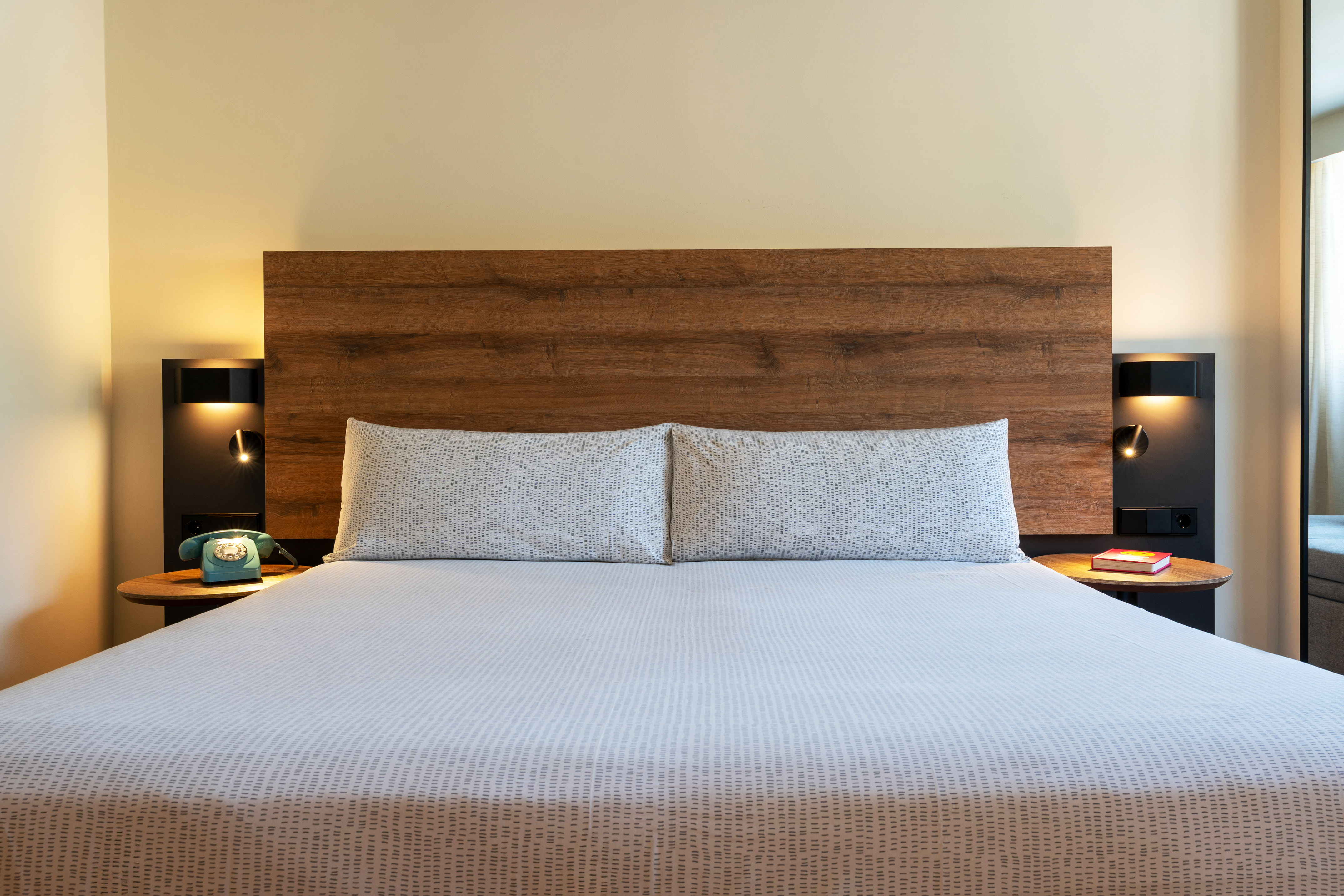Modern hotel room bed with wooden headboard, patterned bedding, and vintage phone.