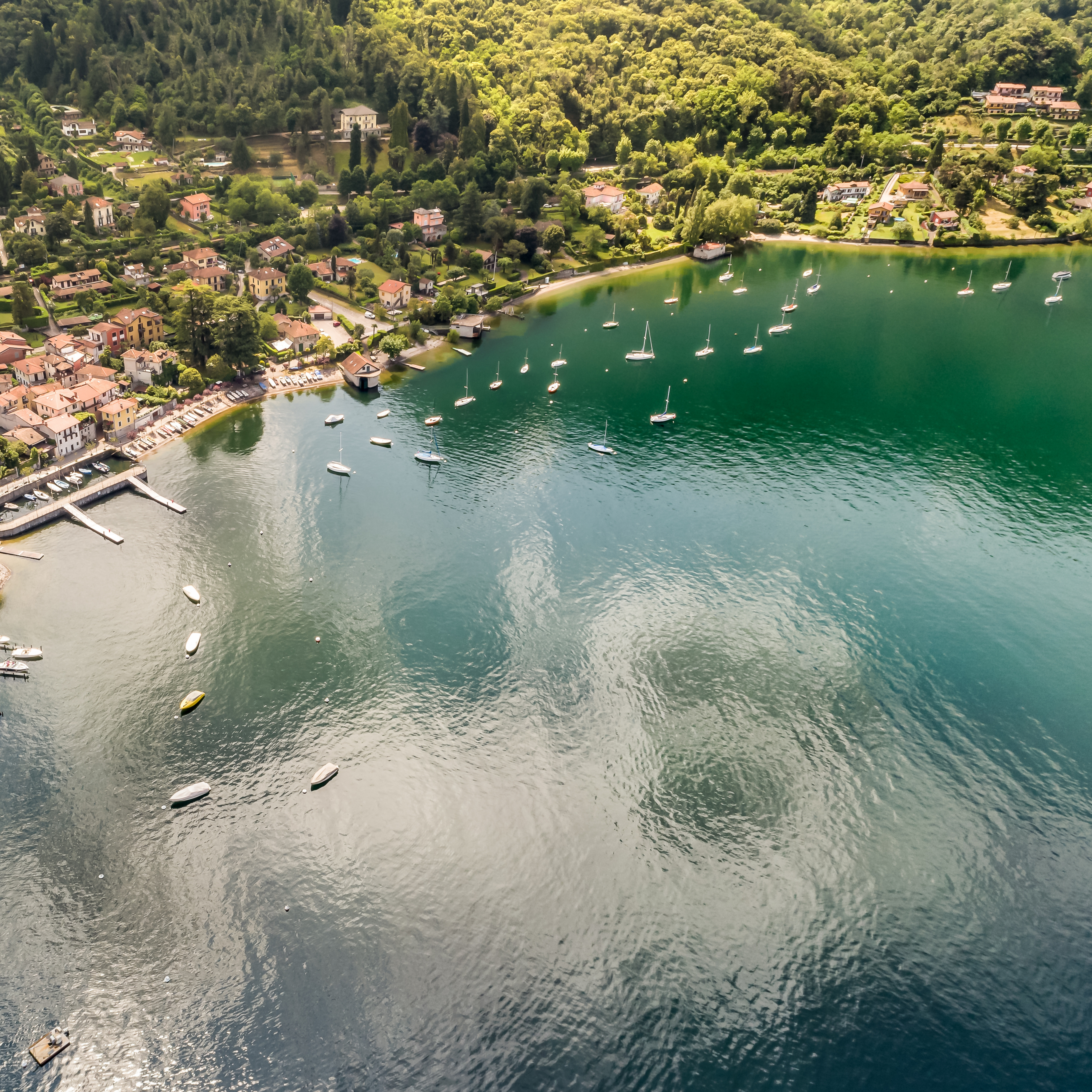 Aerial view of tranquil lake, village shoreline, boats, and lush green hills.