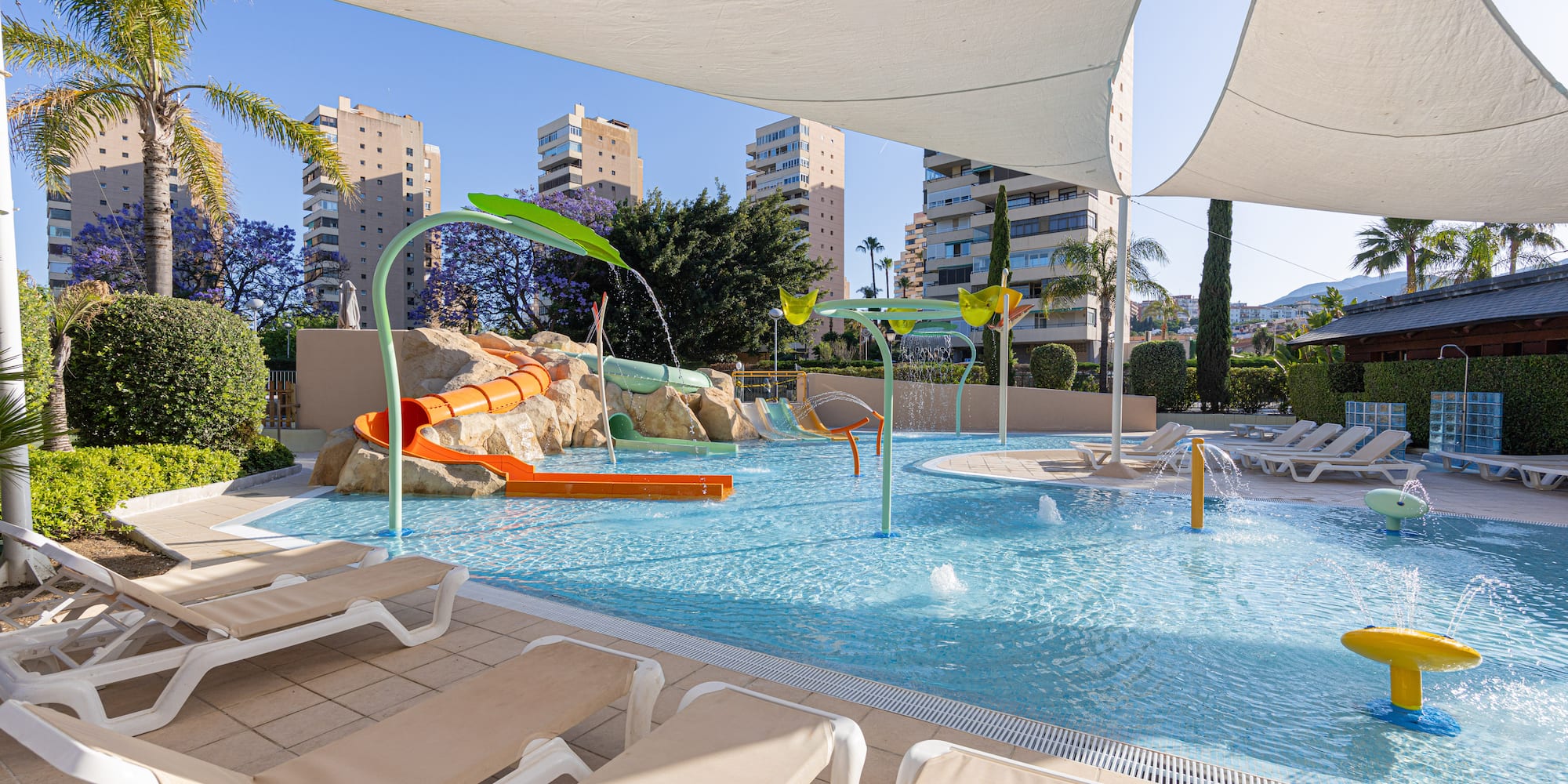 Sunny children's water park with slide, splash pad, lounge chairs.
