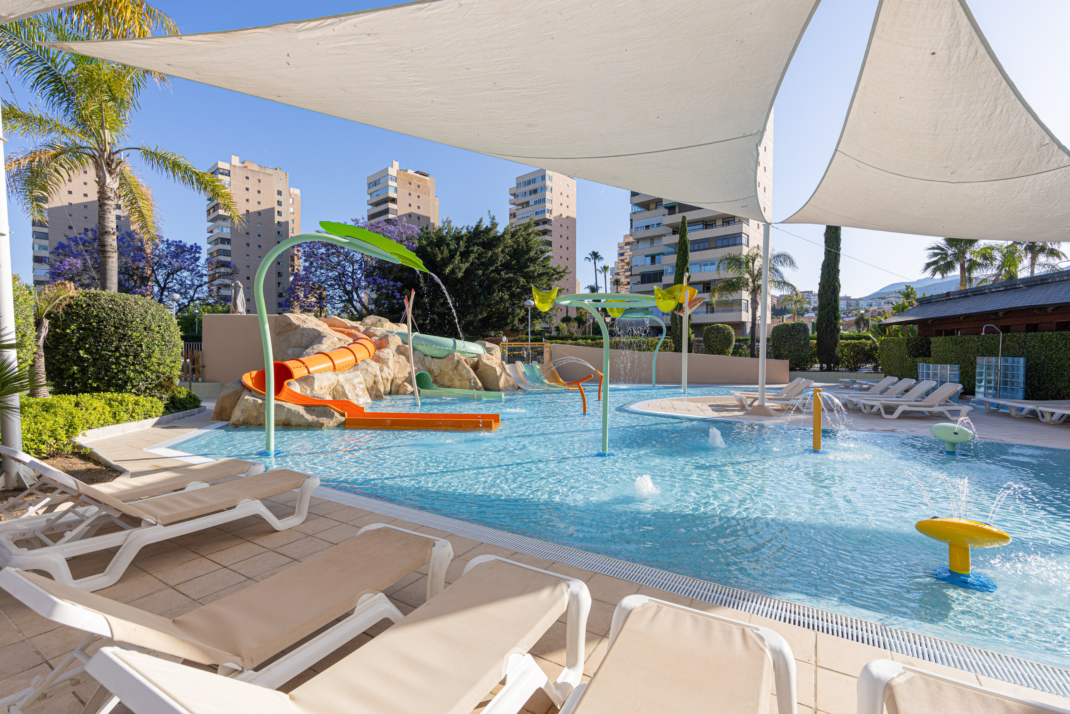 Sunny children's water park with slide, splash pad, lounge chairs.