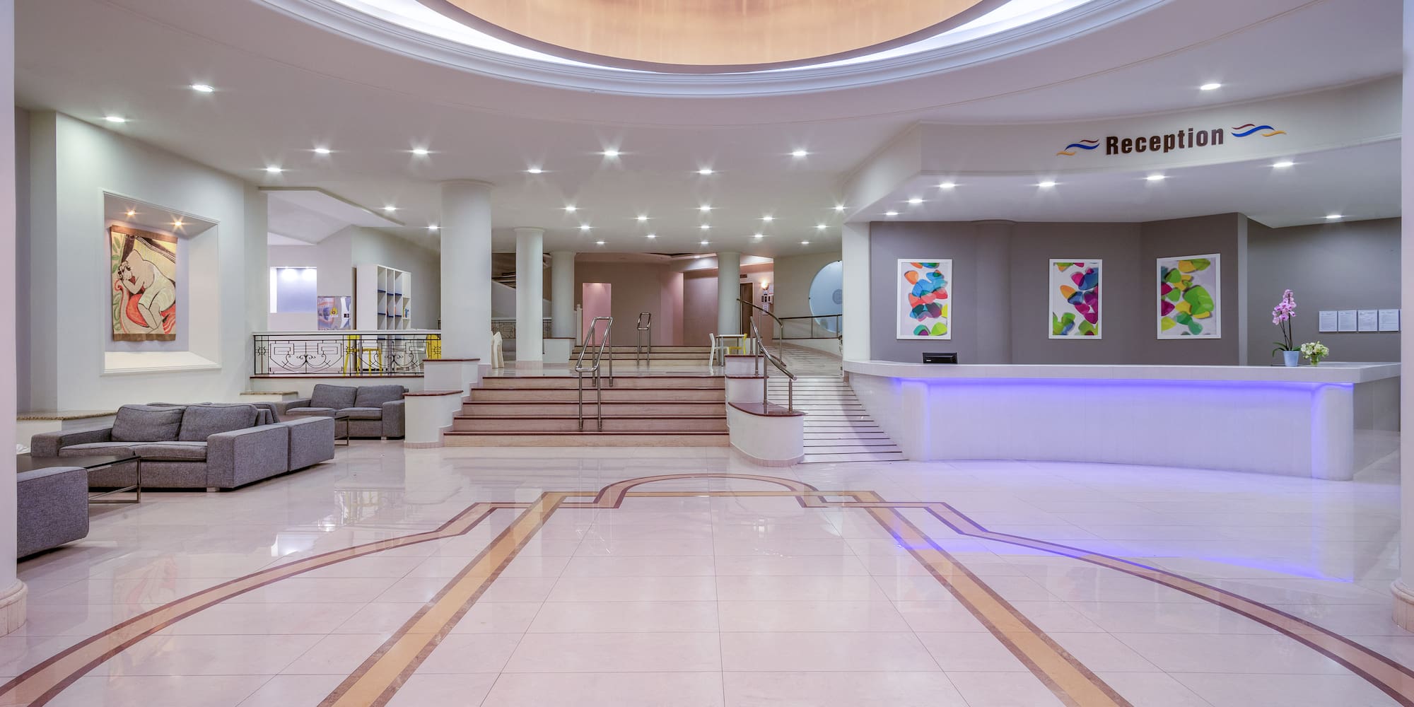 Modern hotel lobby with elegant chandelier, bright reception desk, and seating.