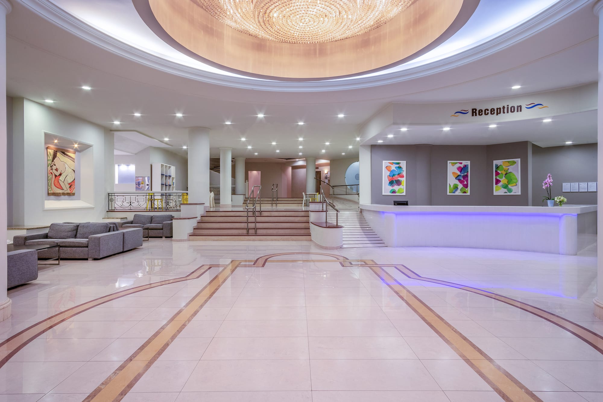 Modern hotel lobby with elegant chandelier, bright reception desk, and seating.