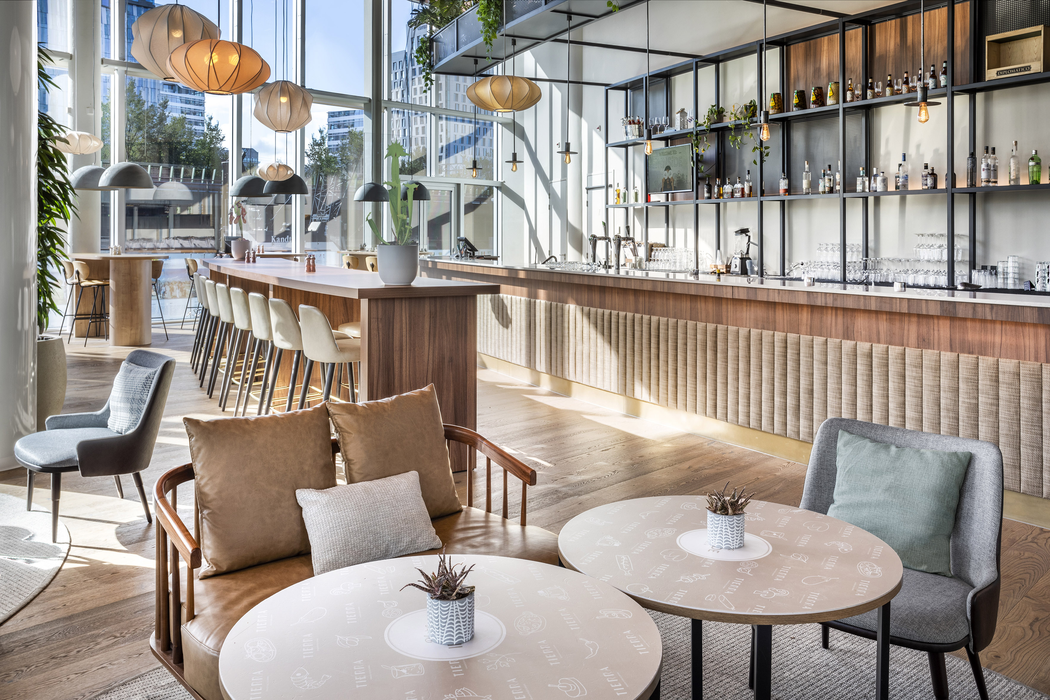 Modern bar and lounge with natural light, stylish lamps, and comfortable seating.