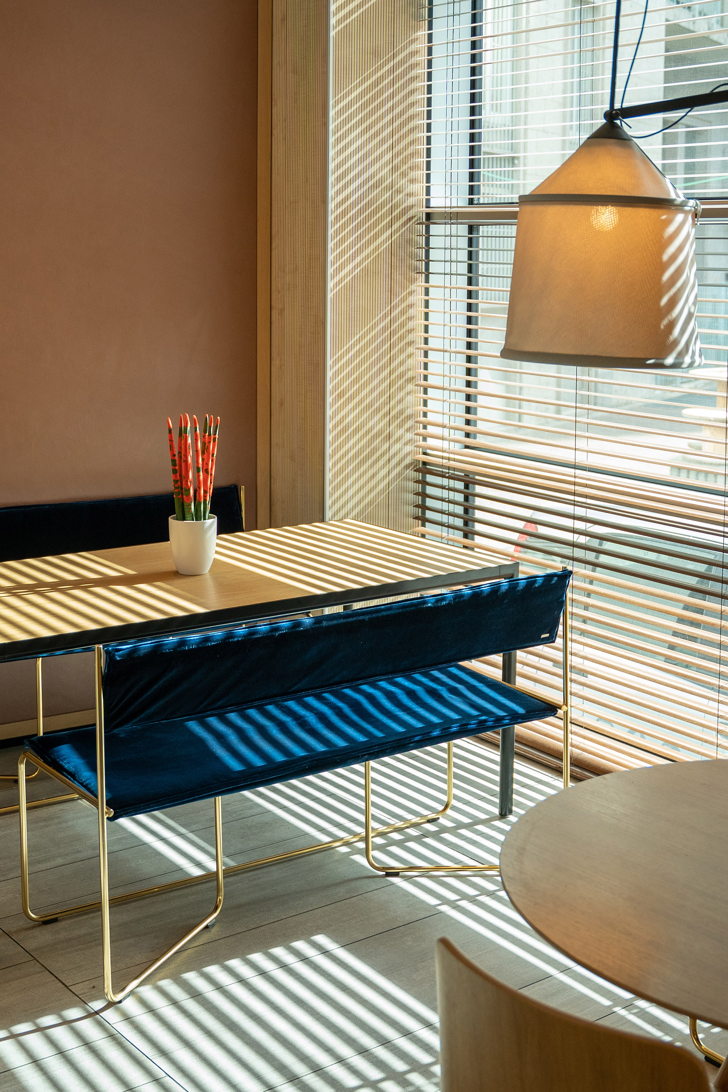 Sunlit modern dining area with blue velvet bench and wooden table.