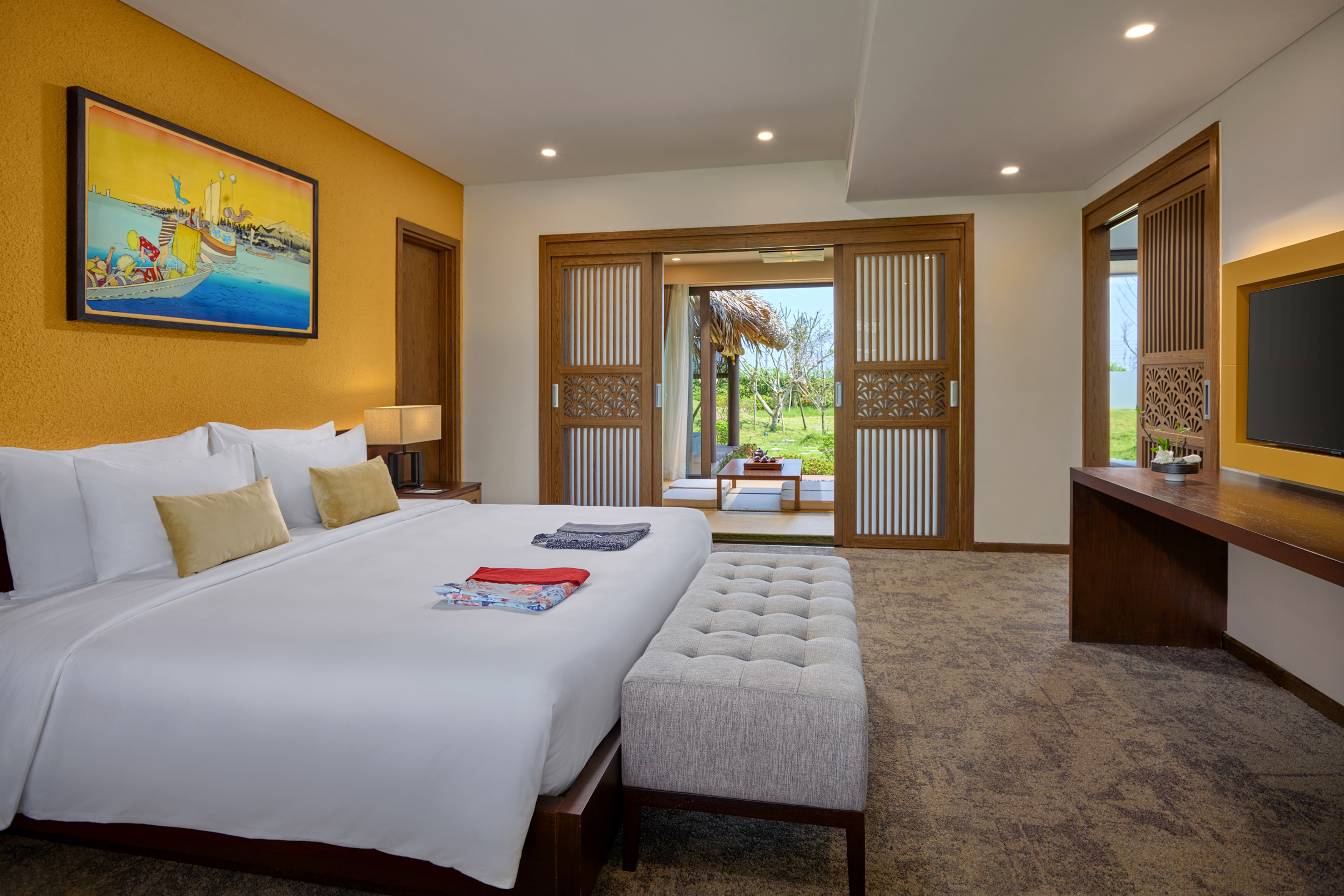 Modern hotel bedroom with king bed, yellow wall, and garden patio view.
