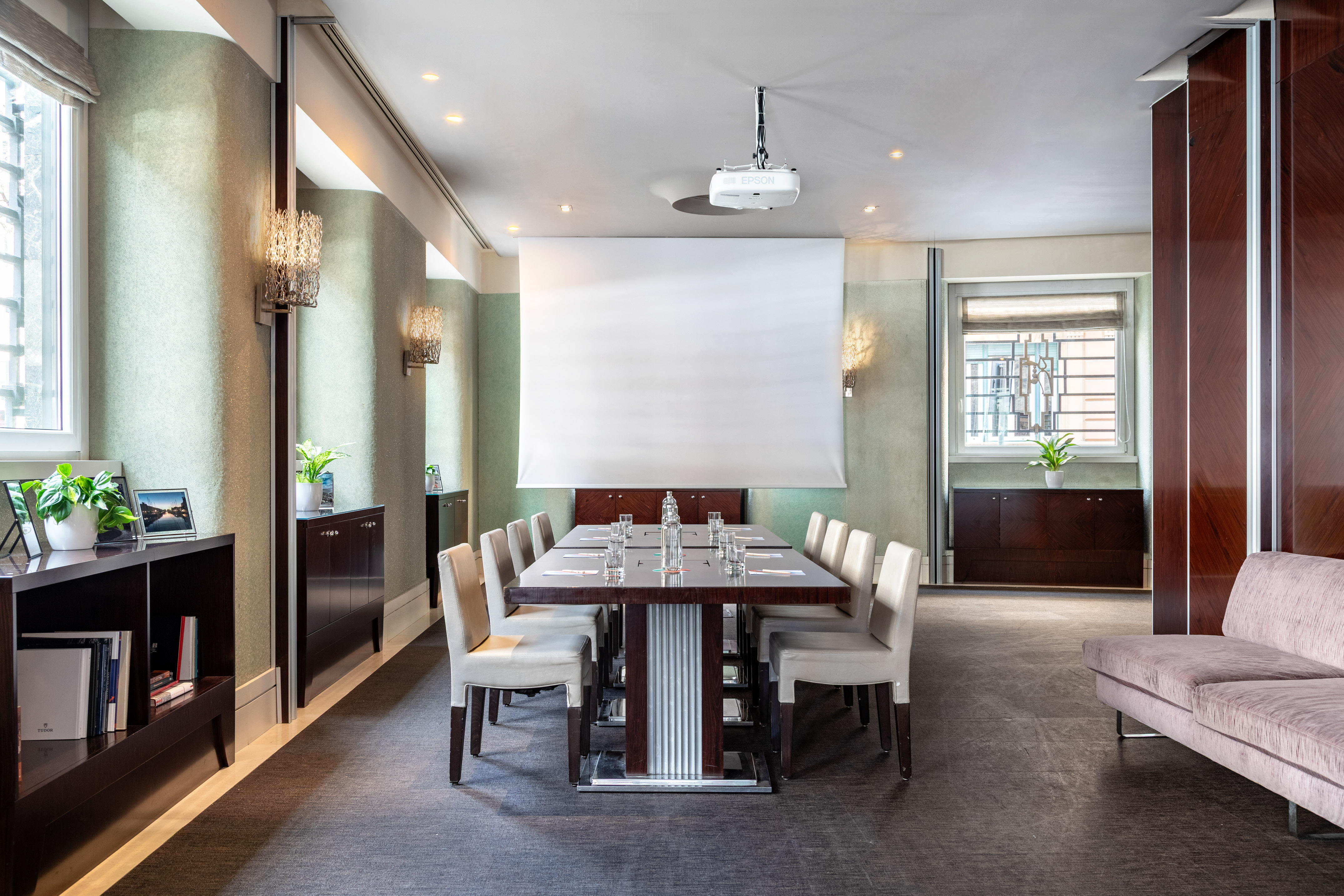 Elegant boardroom with projector, screen, long table, chairs, and stylish lighting.