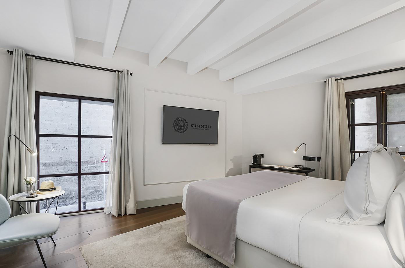 Bright modern hotel bedroom with large bed, wall TV, wood floor, and large windows.