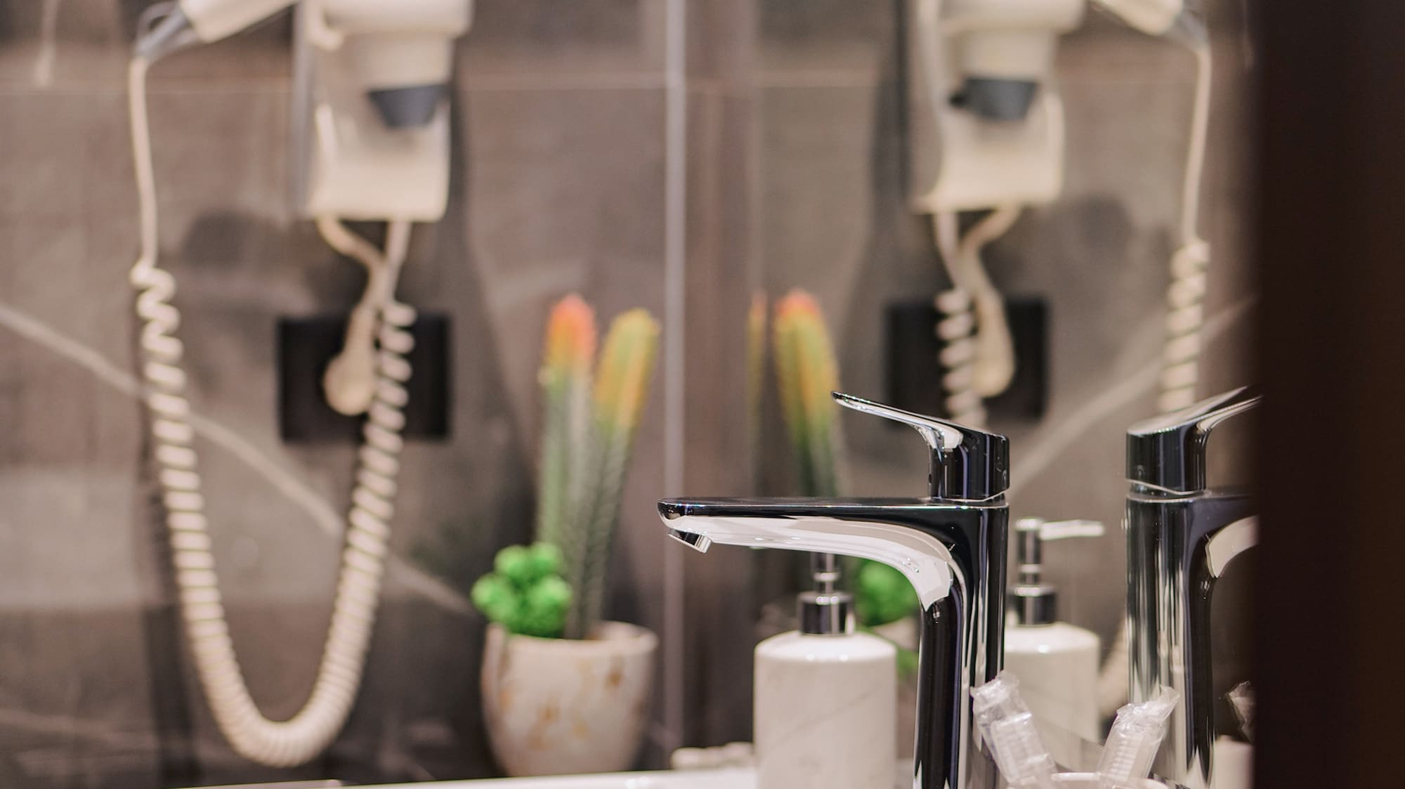 Modern bathroom vanity with white sink, chrome faucet, hairdryer, and plants.