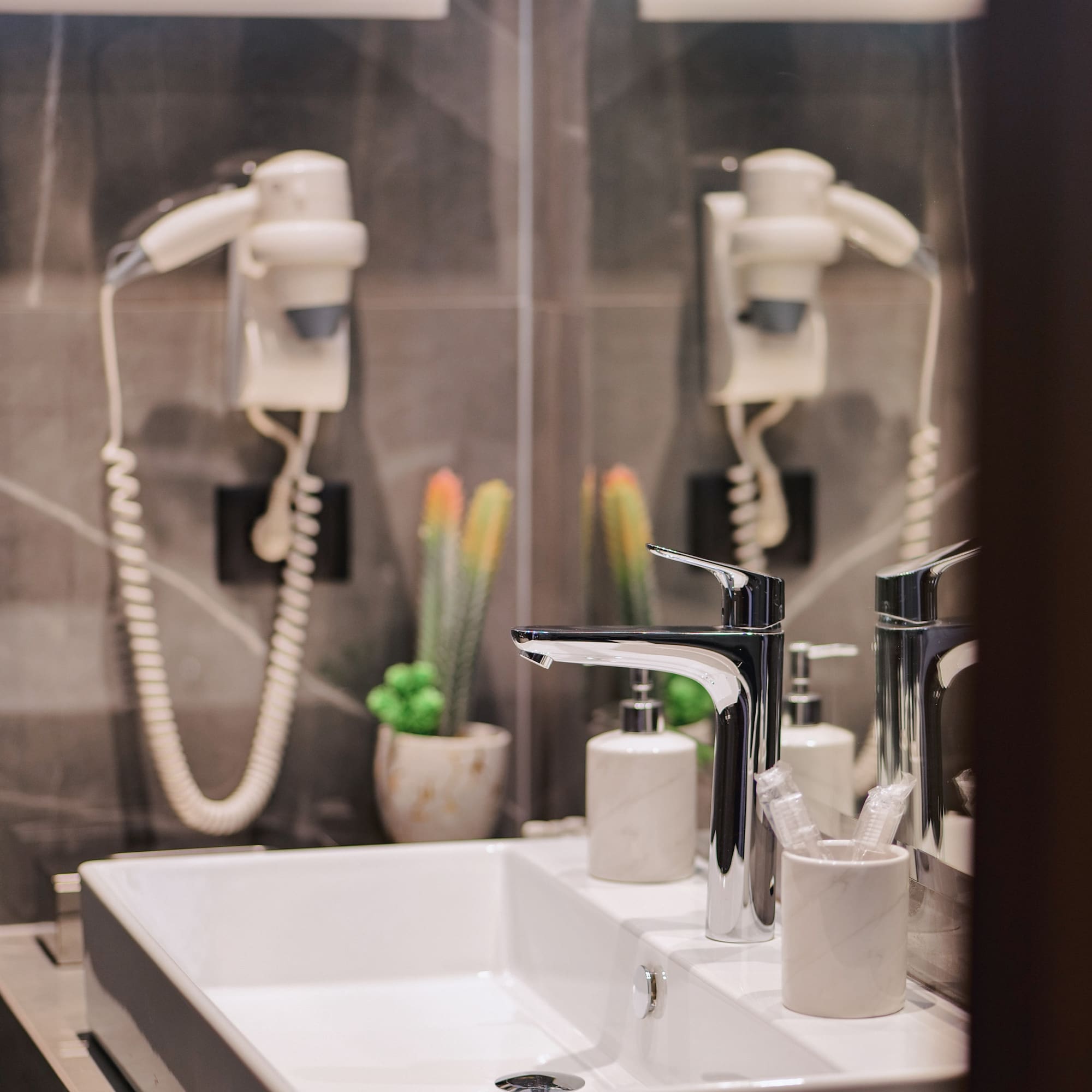 Modern bathroom vanity with white sink, chrome faucet, hairdryer, and plants.