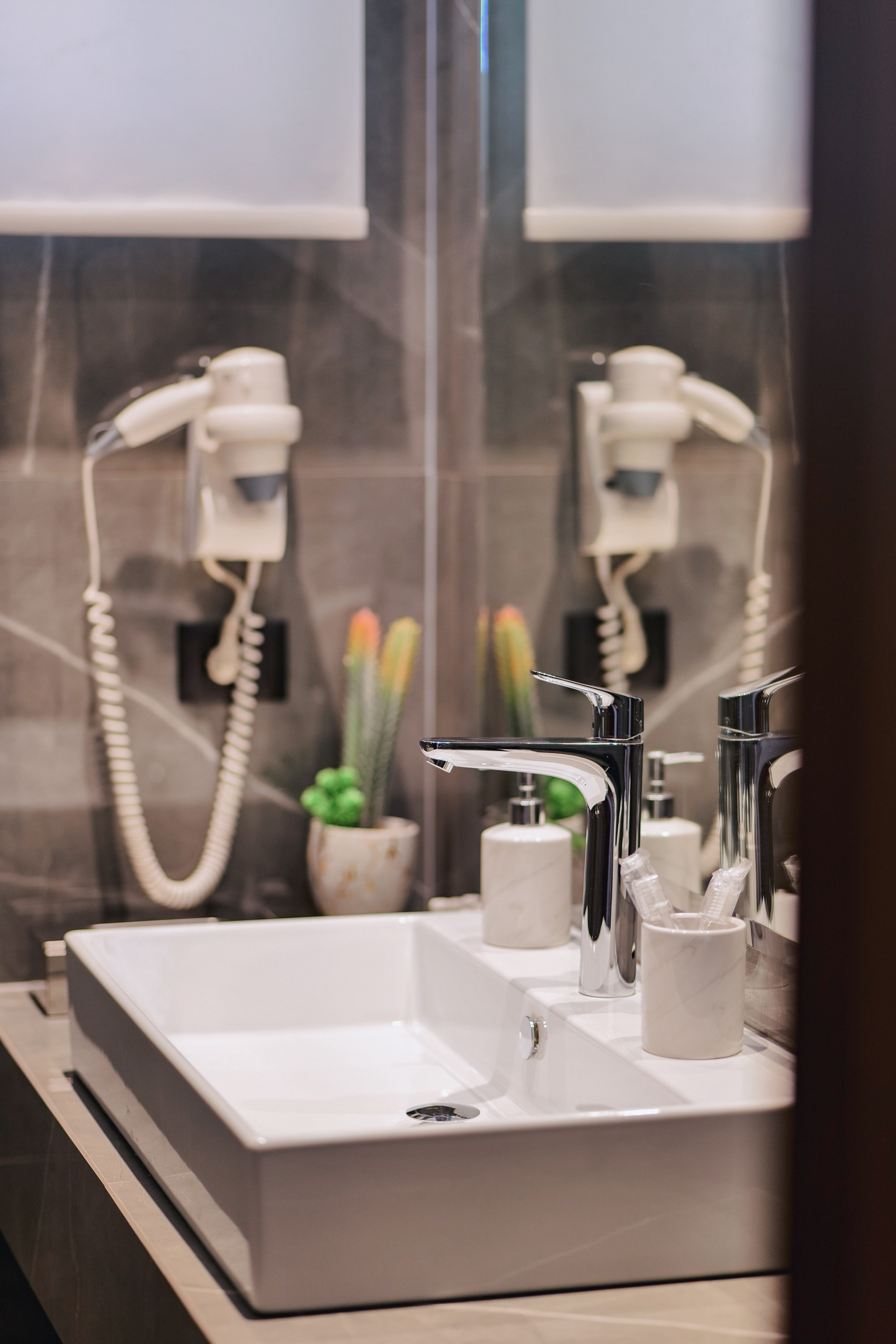Modern bathroom vanity with white sink, chrome faucet, hairdryer, and plants.