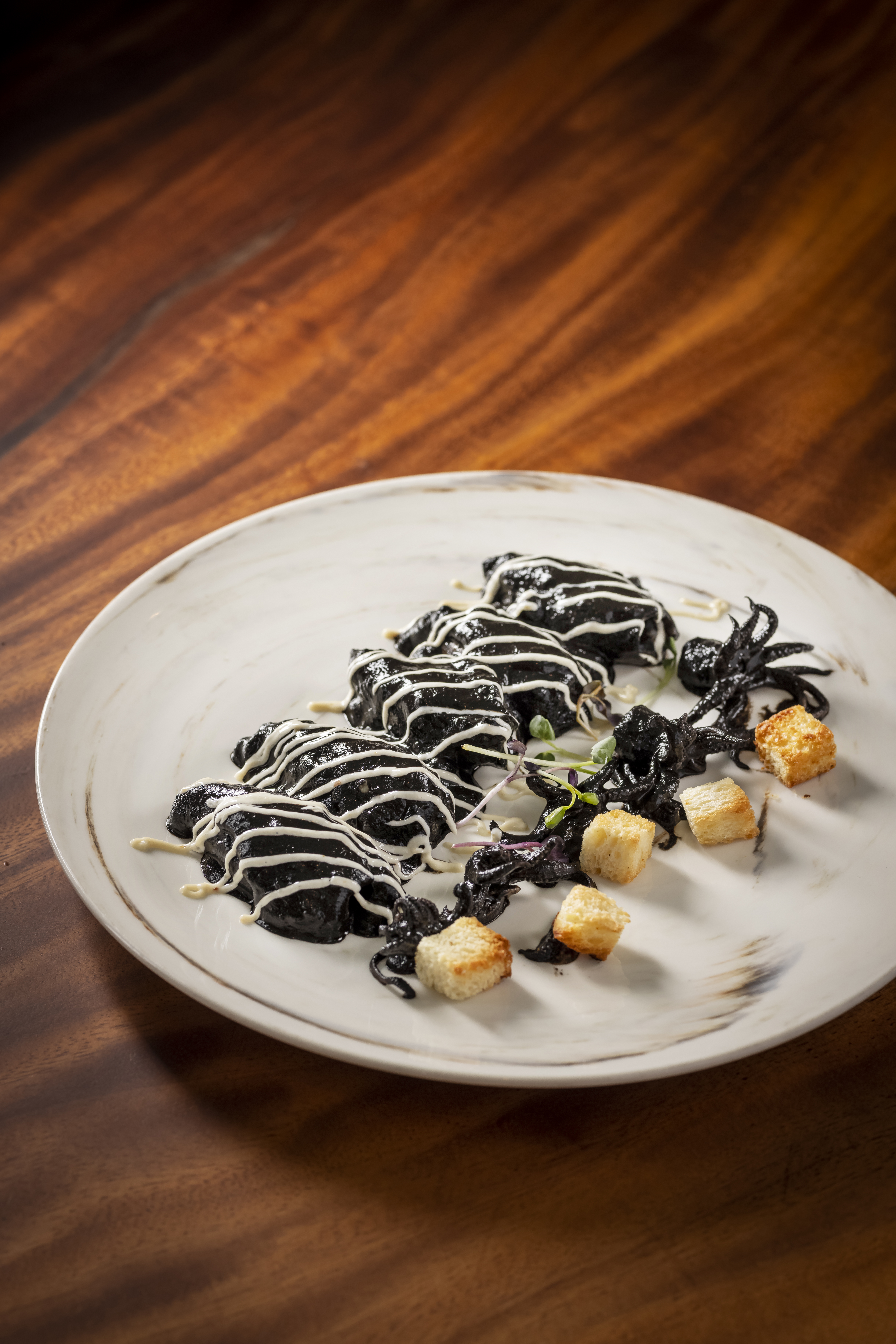 Black squid ink dish with white sauce, tentacles, croutons, and greens.