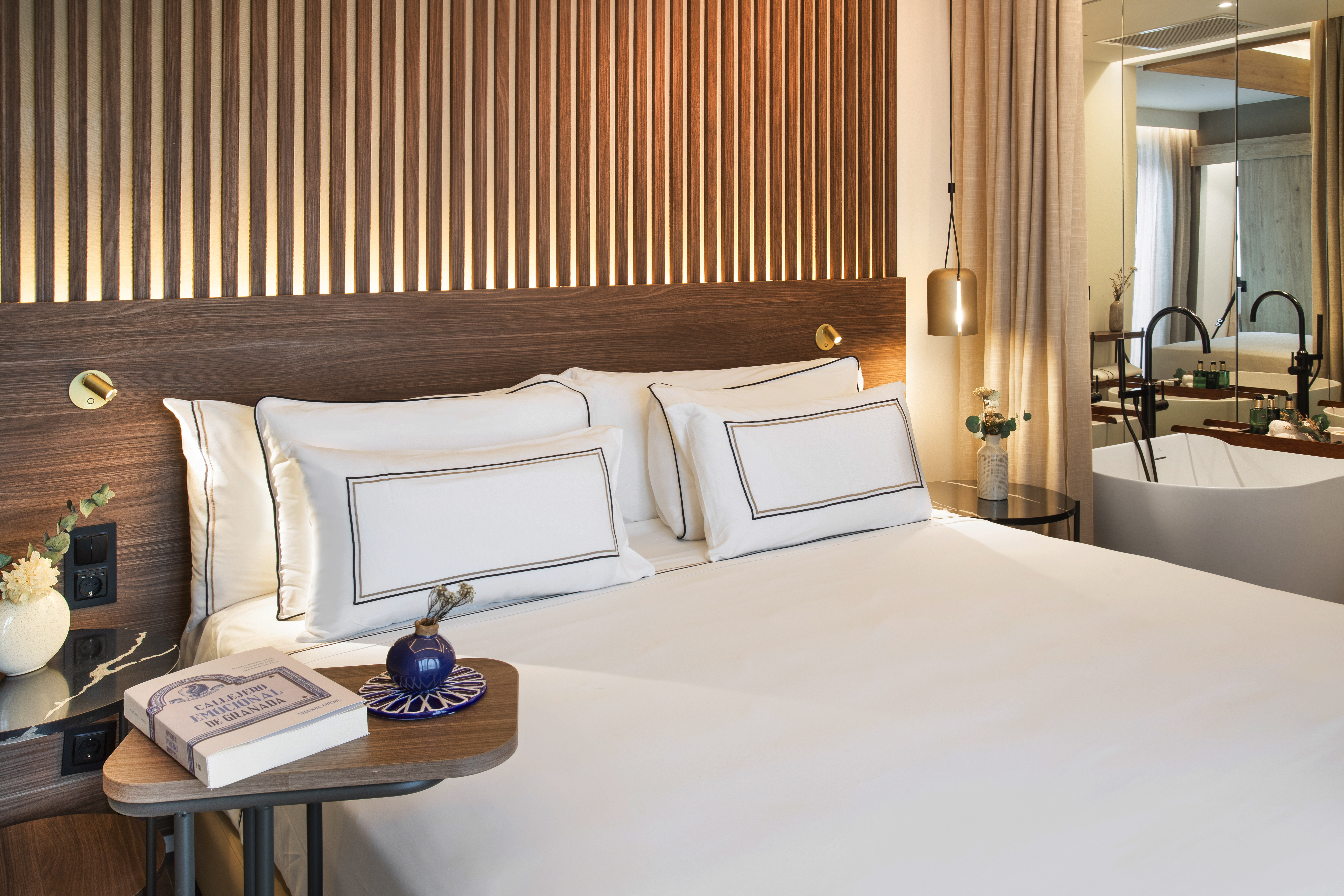 Luxury hotel room: modern bed, wood-slat headboard, freestanding bathtub.