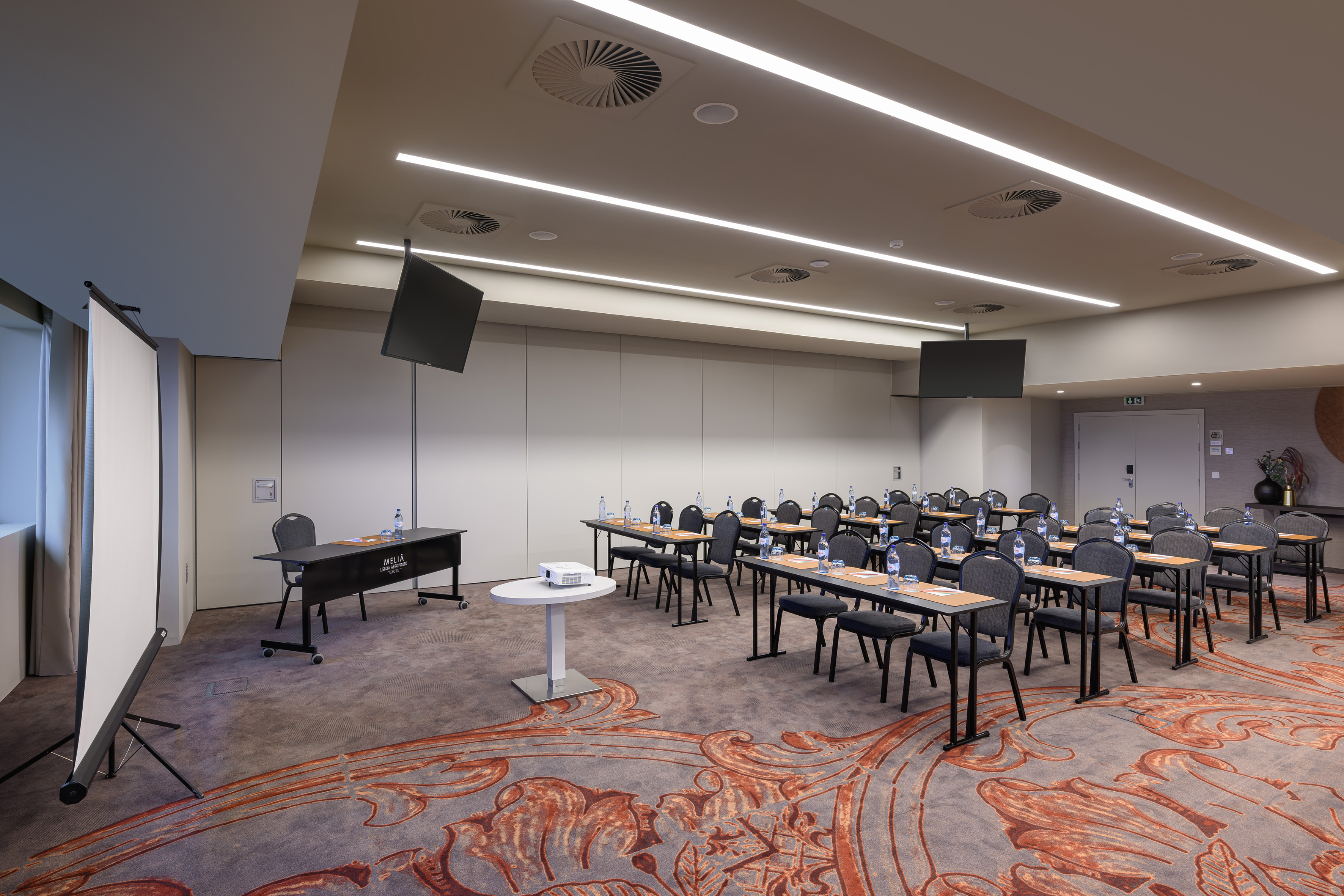Modern conference room with tables, chairs, projector, and presentation screens.