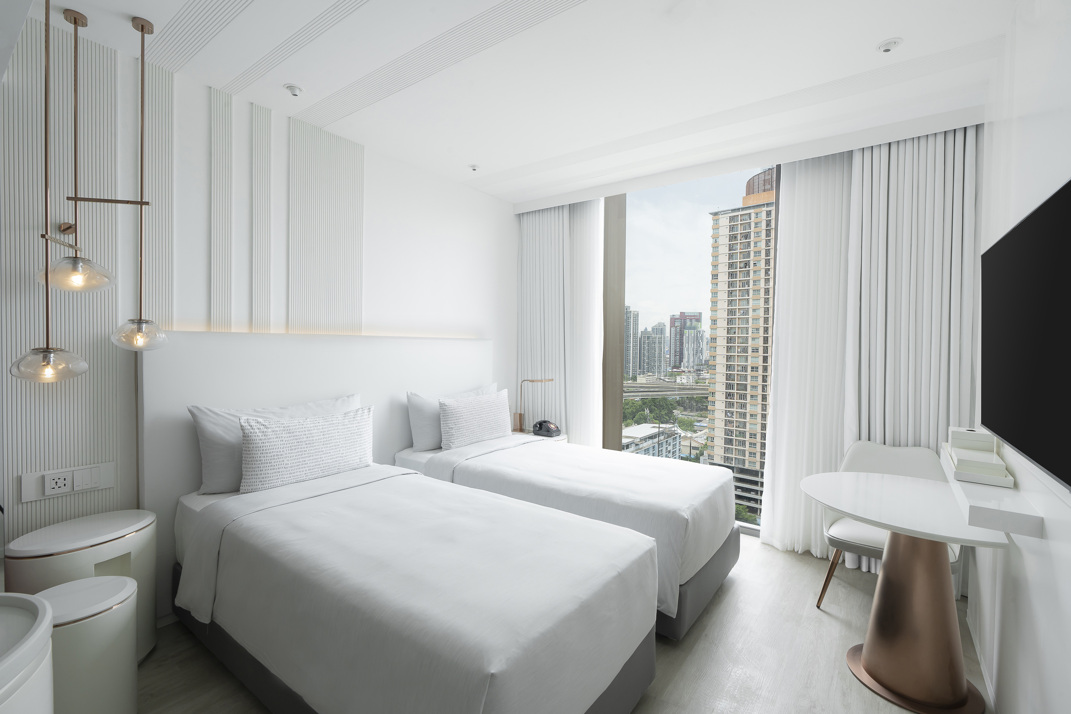 Modern hotel room with twin beds, city view, and white decor.