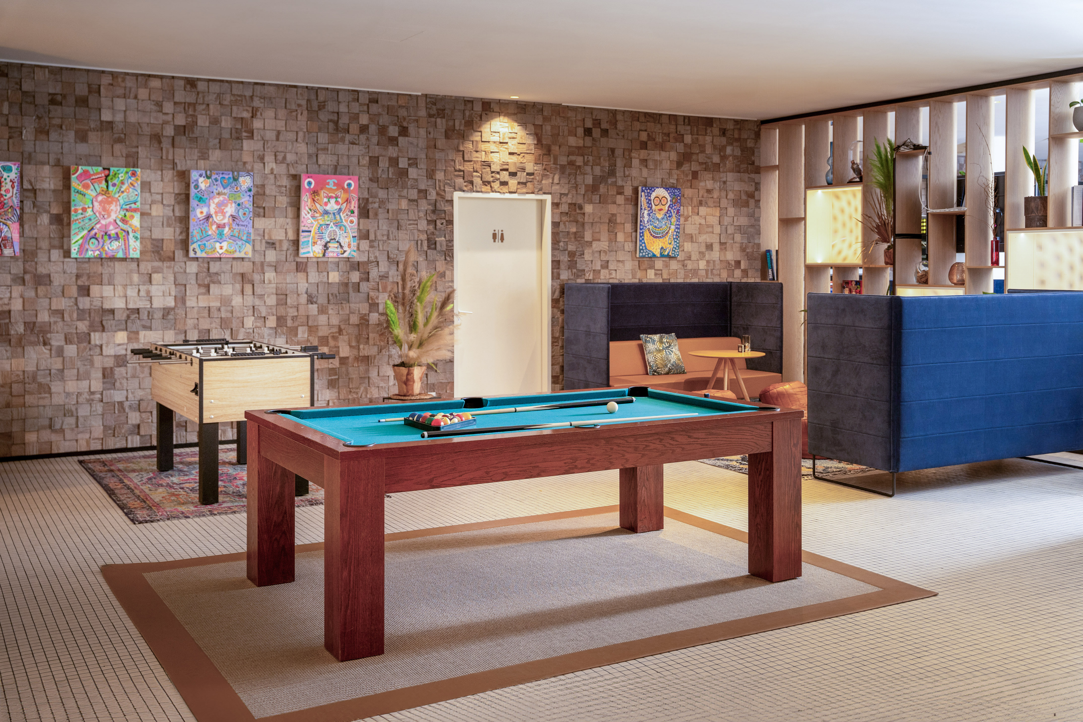 Modern game room with pool table, foosball, colorful art, and lounge seating.