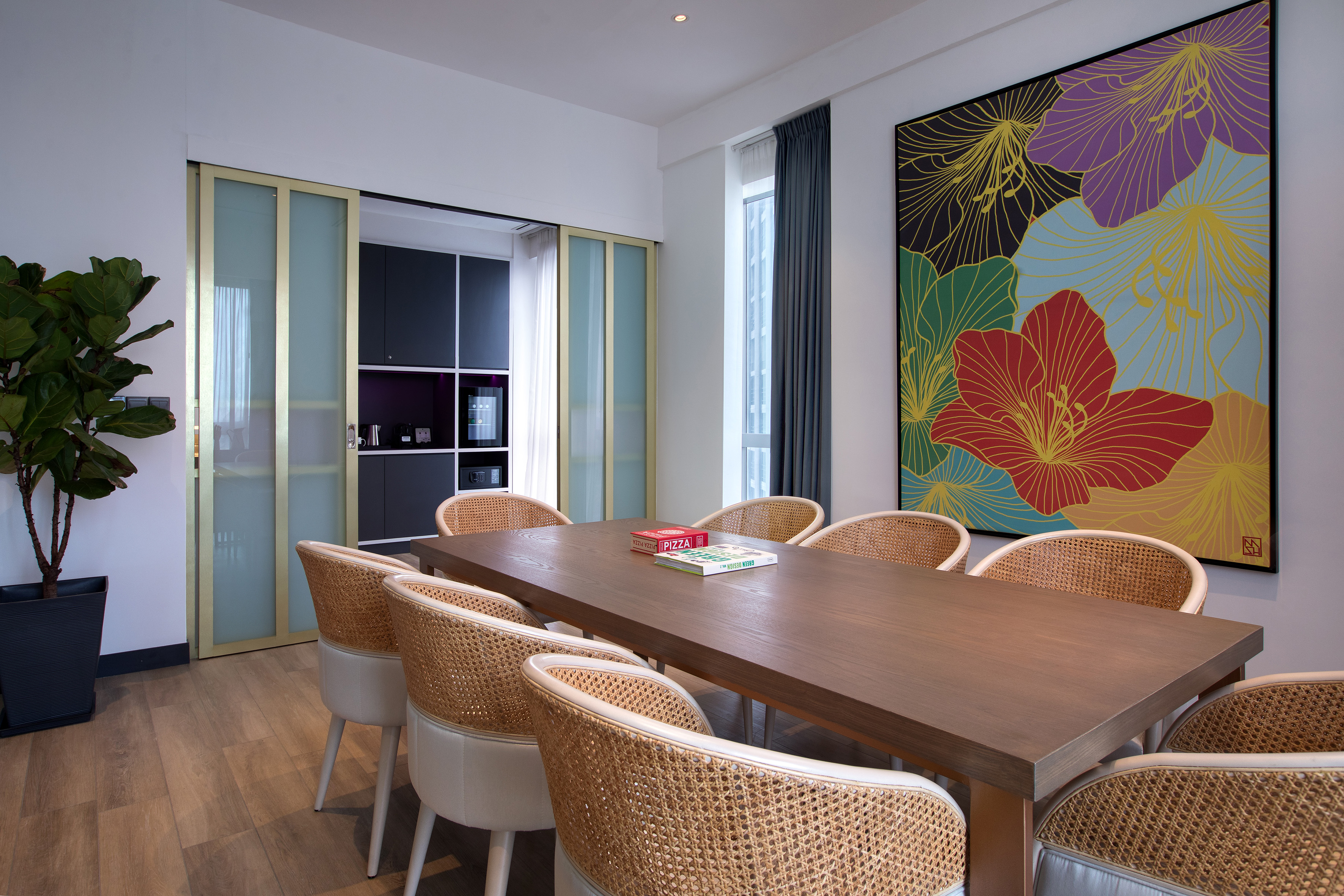 Modern dining area, wood table, wicker chairs, floral art, kitchenette.