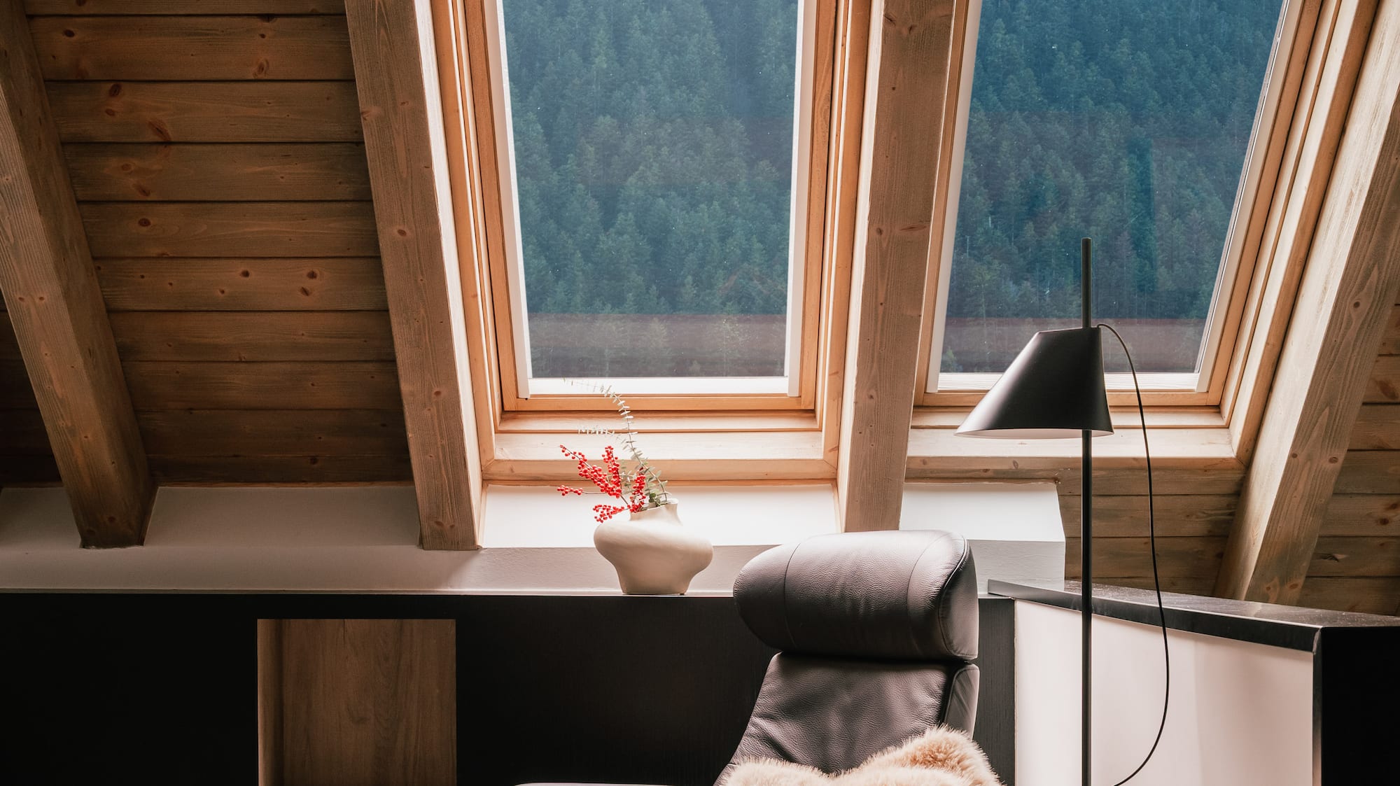 Cozy attic lounge with leather chair, ottoman, skylights, and forest view.