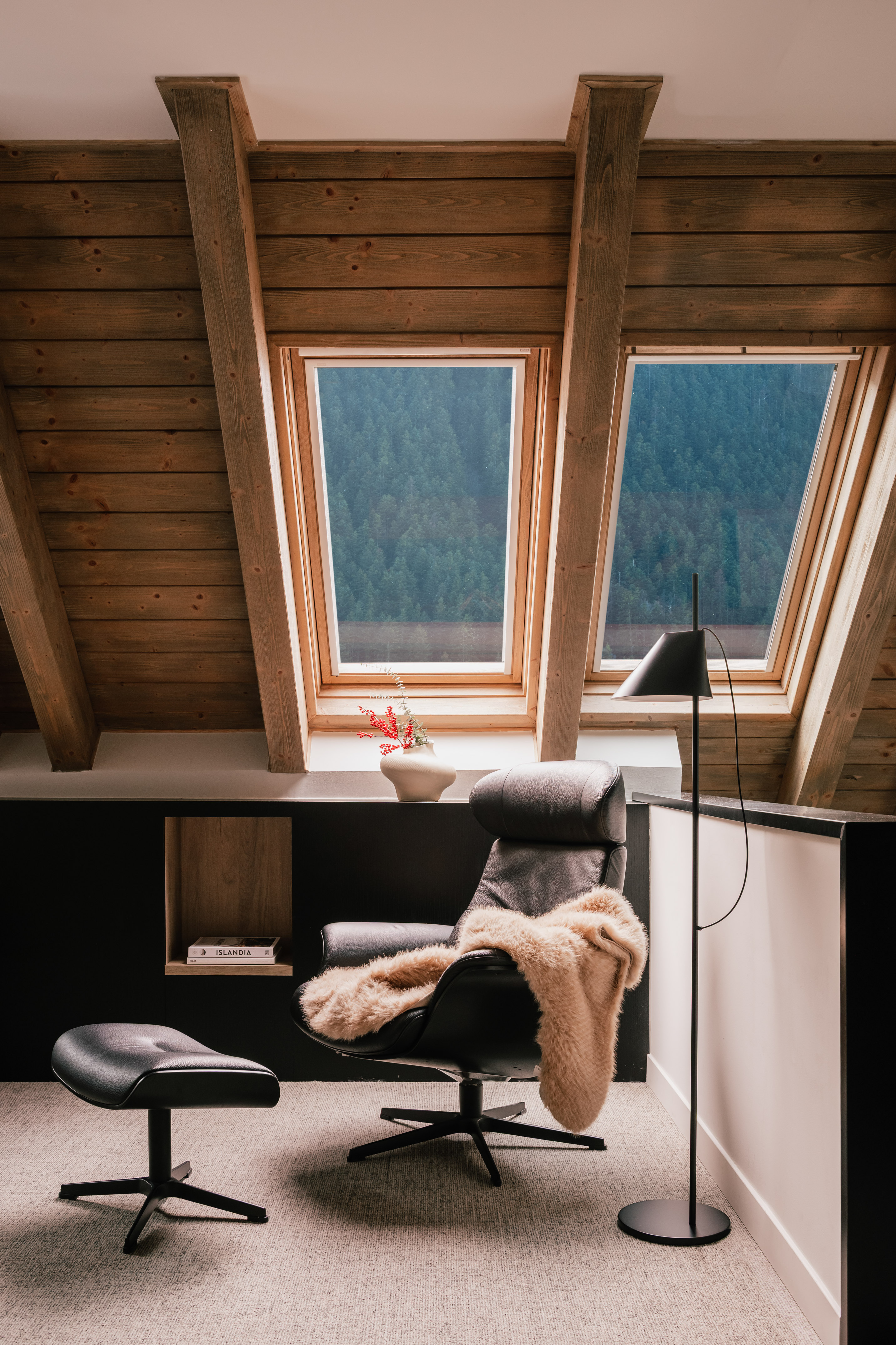 Cozy attic lounge with leather chair, ottoman, skylights, and forest view.