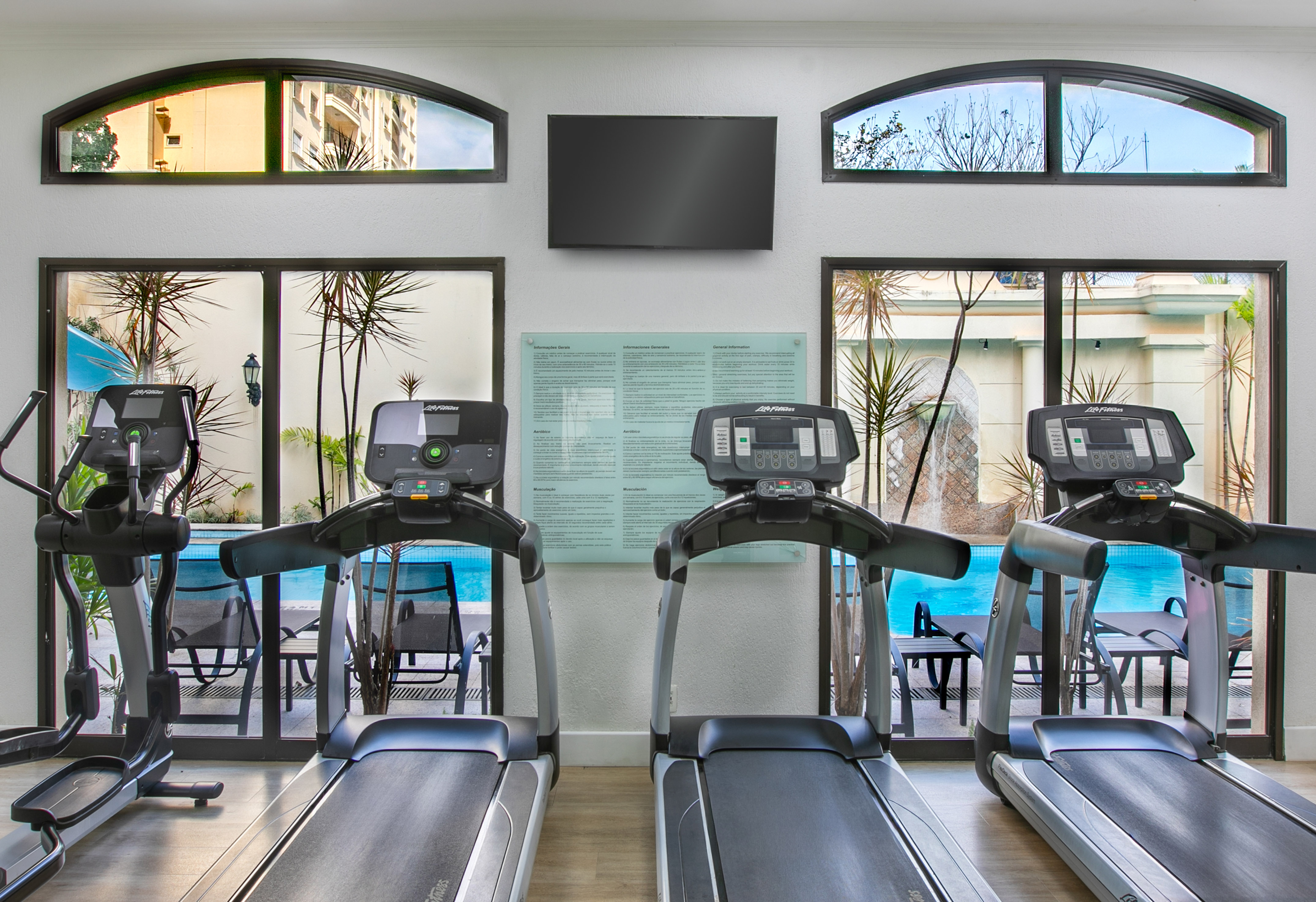 Gym with Life Fitness treadmills, elliptical, large windows, and outdoor pool view.