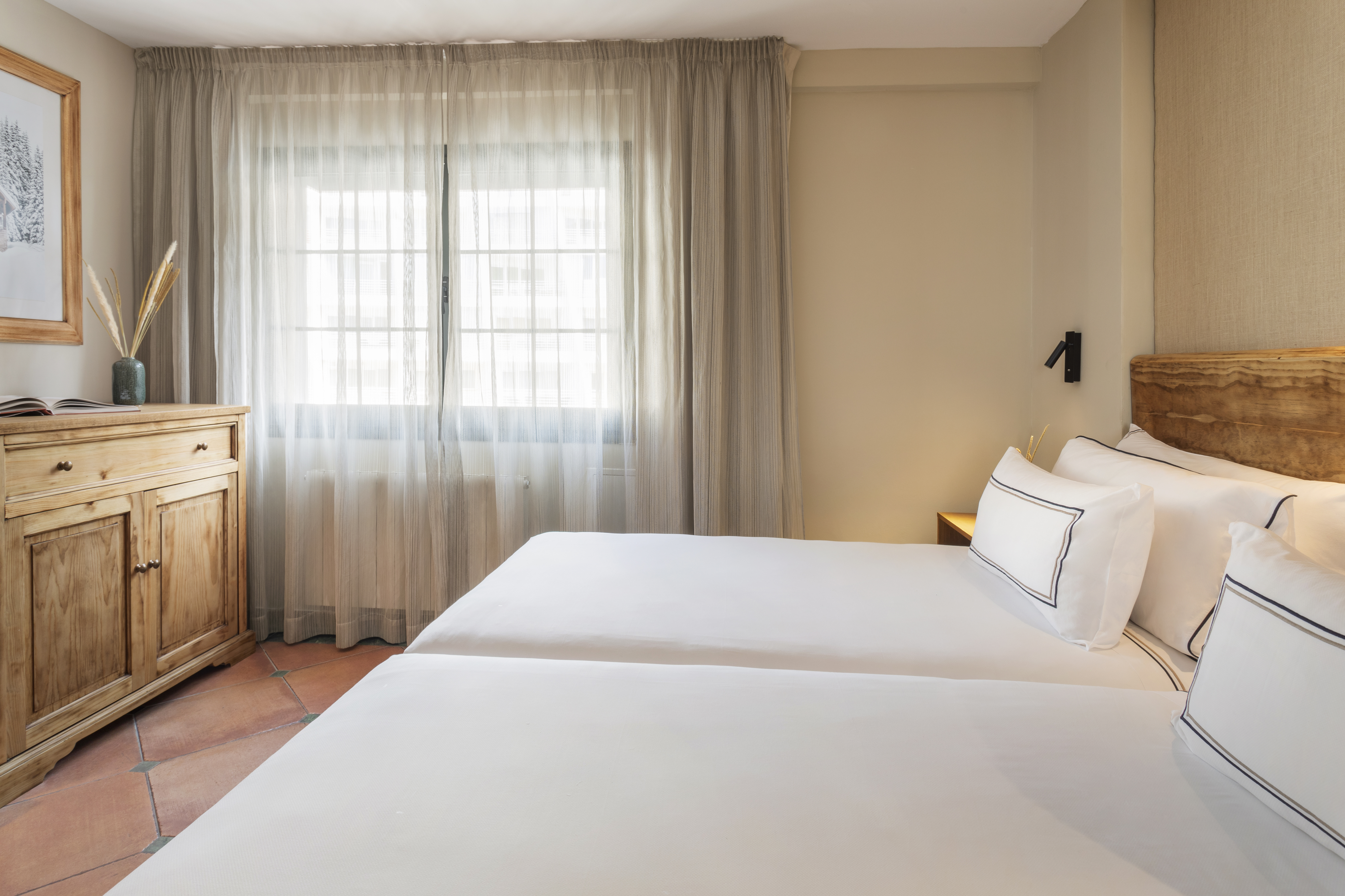 Cozy twin bedroom with white beds, wooden furniture, tiled floor, and window.