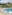 Tropical beach with people swimming, hillside village, palm trees, and blue ocean.