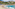 Tropical beach with people swimming, hillside village, palm trees, and blue ocean.