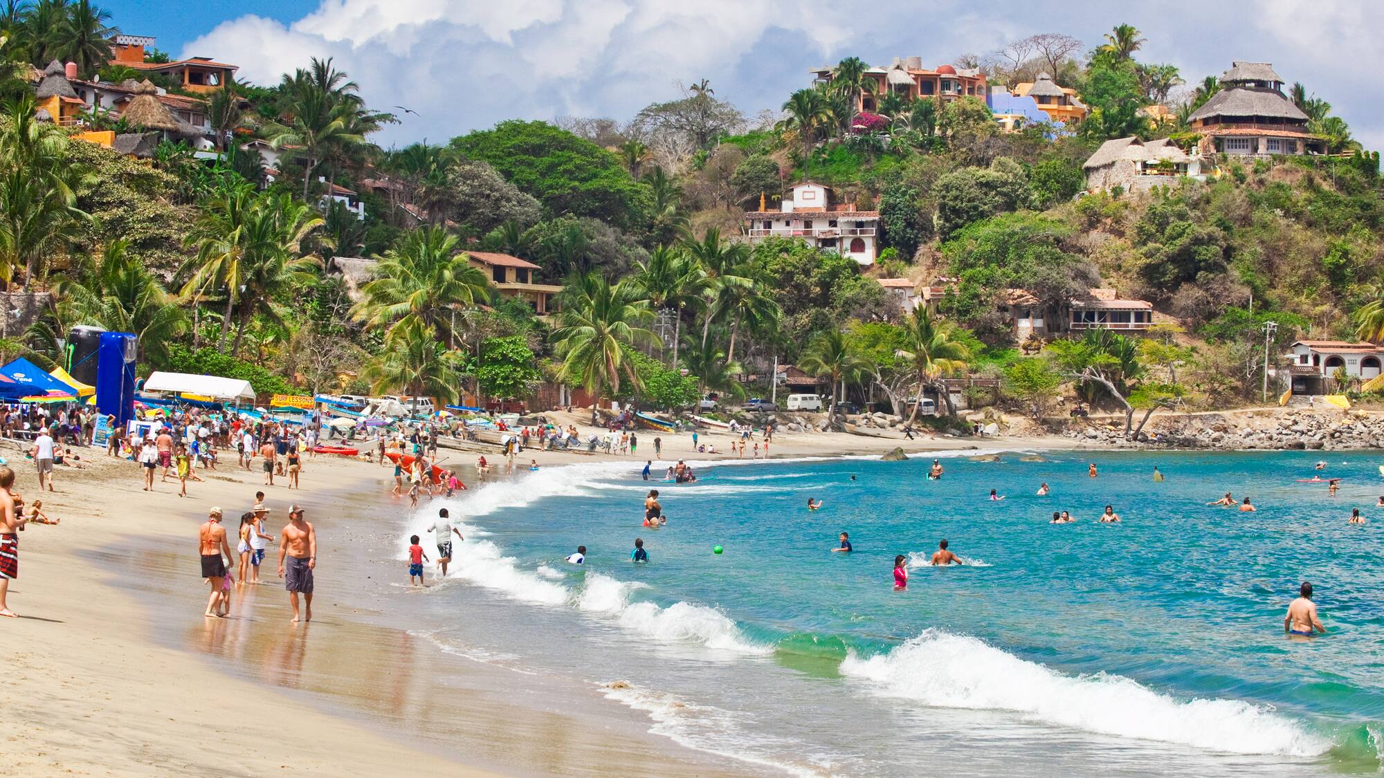 a beach with people and houses on the hill
