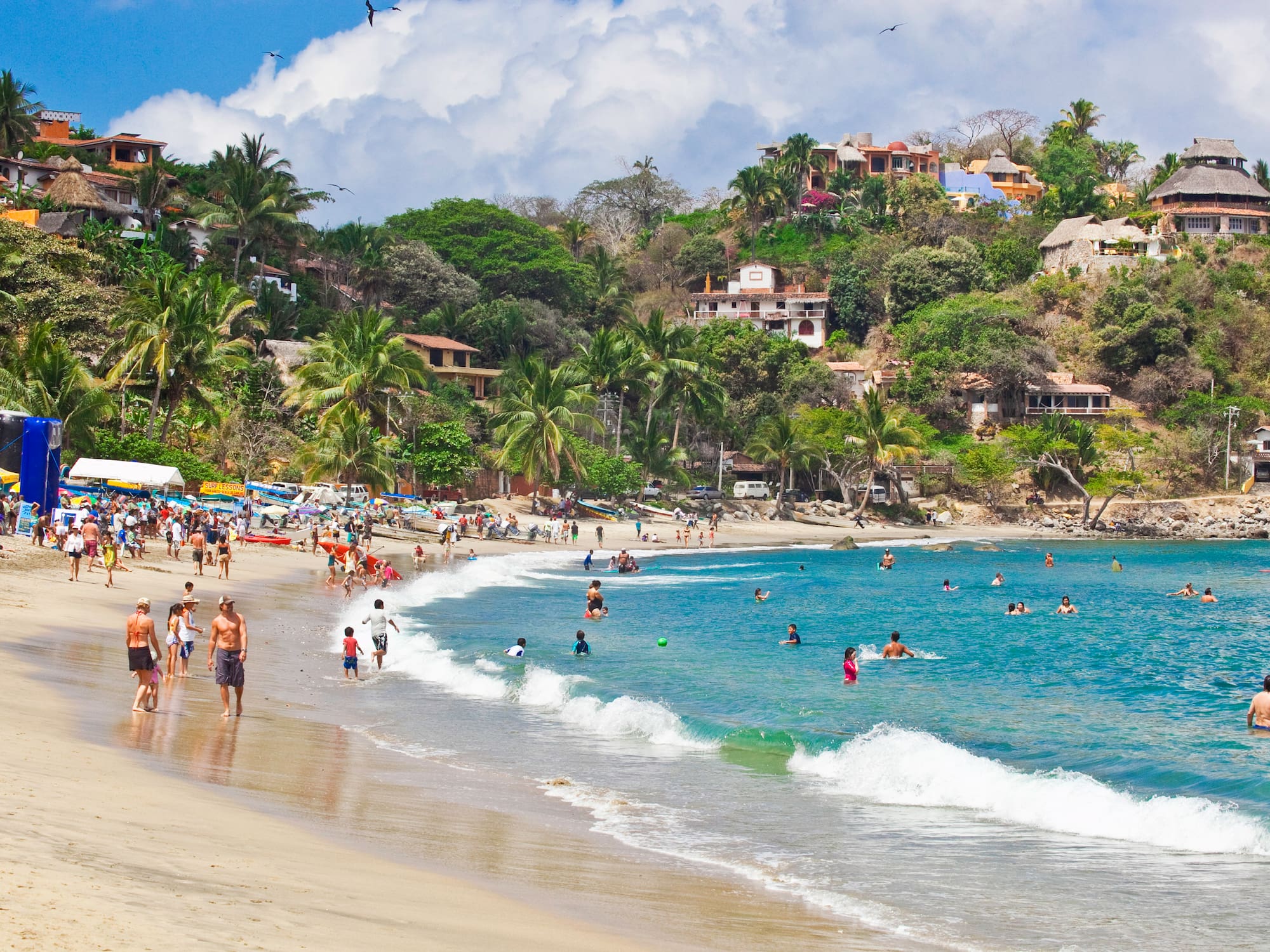a beach with people and houses on the hill