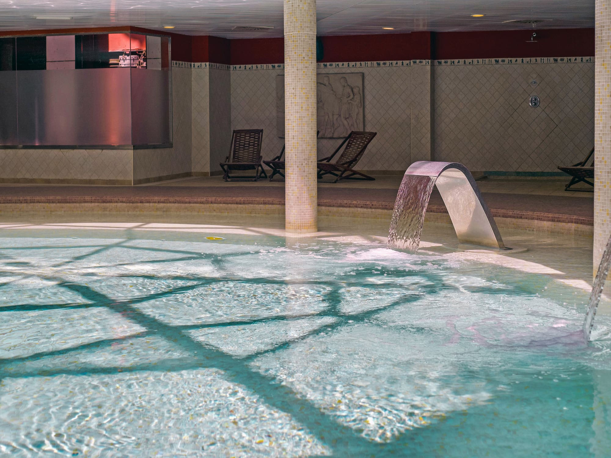 Piscina interior de spa con cascadas de agua y tumbonas.