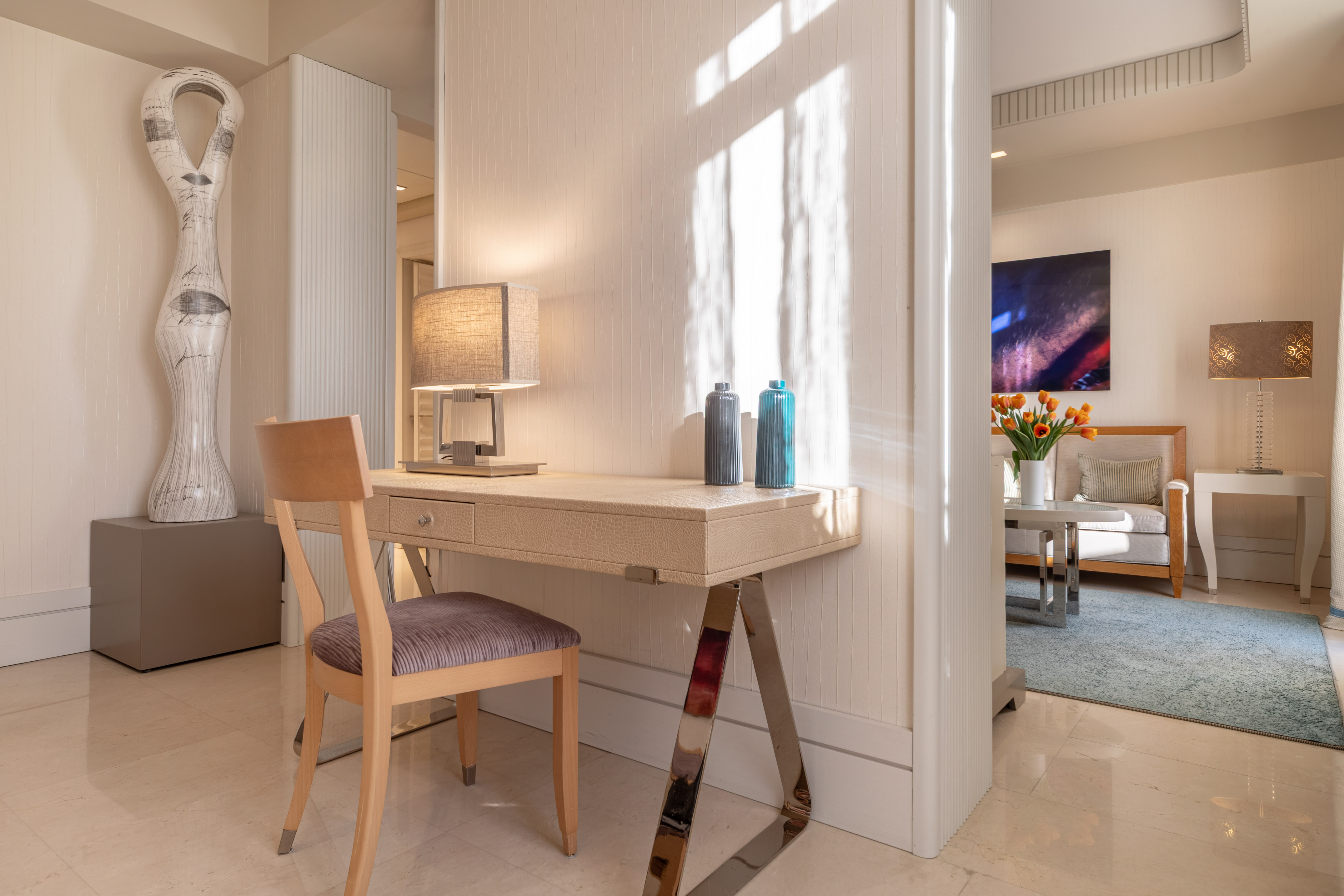 Modern home office with elegant desk, chair, lamp, and abstract sculpture.