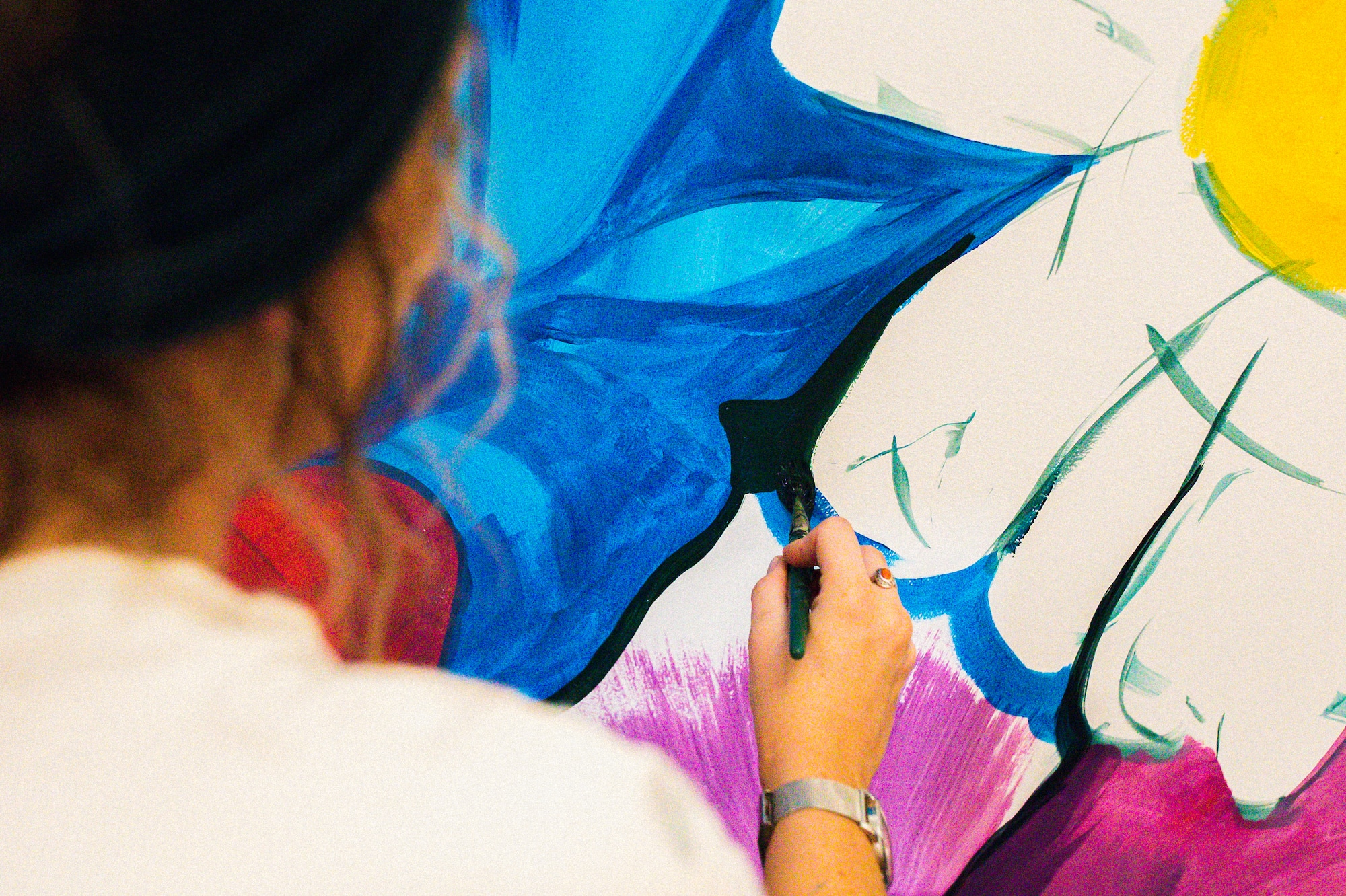 Artist's hand painting vibrant blue, purple, yellow floral art on canvas.
