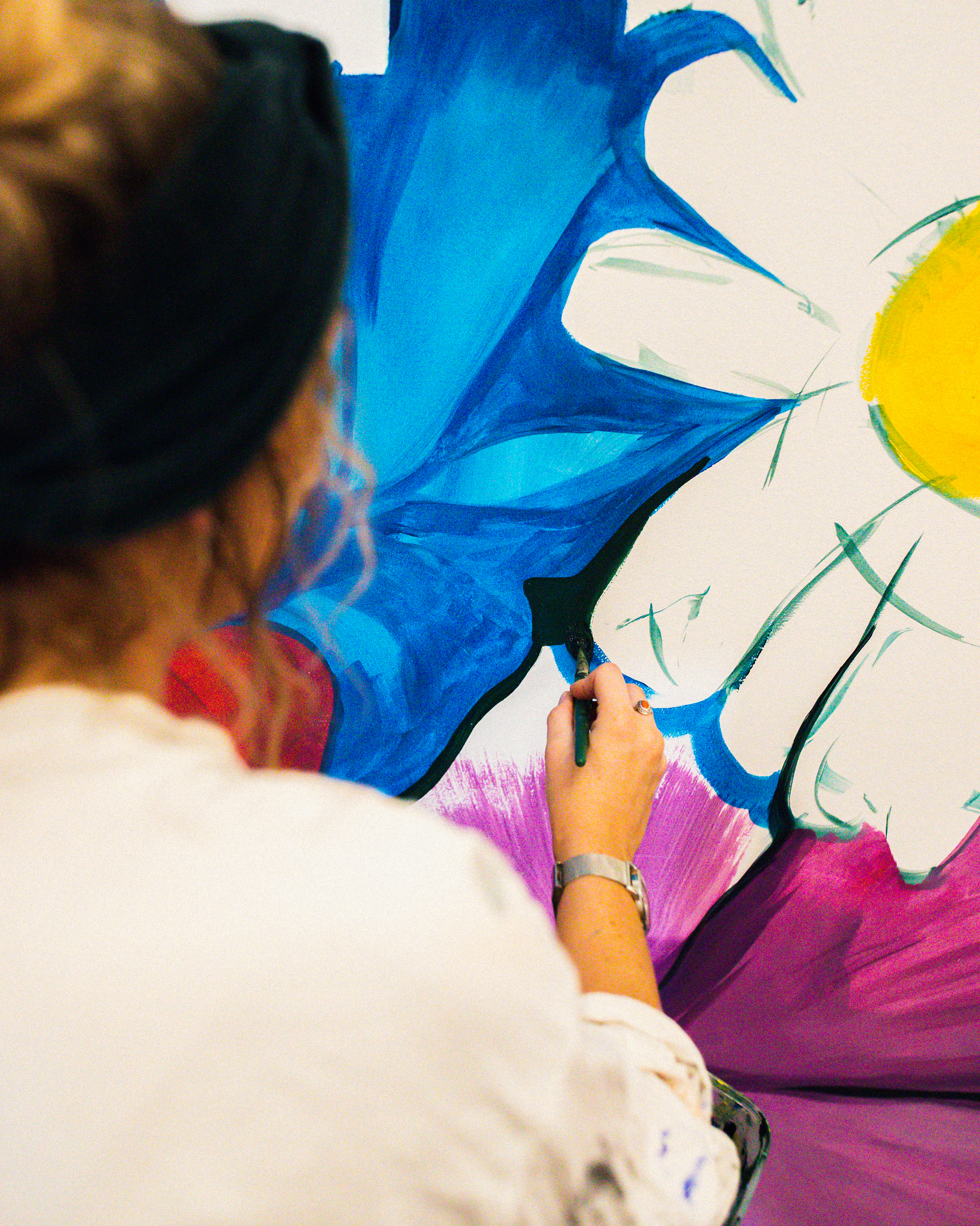 Artist's hand painting vibrant blue, purple, yellow floral art on canvas.