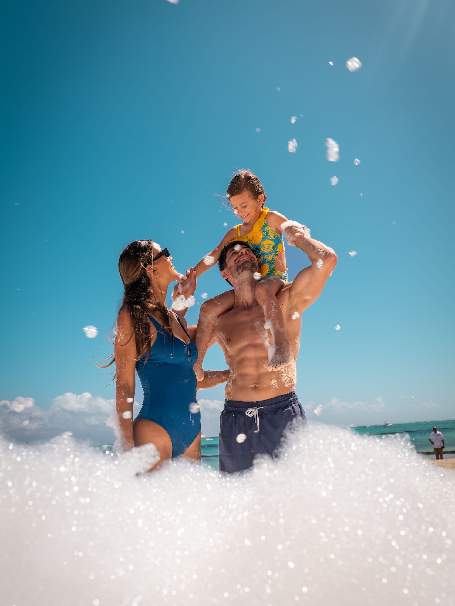 a man and woman with a child on his shoulders on a beach
