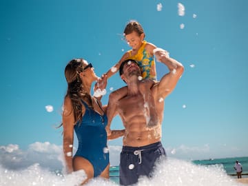 a man and woman with a child on his shoulders on a beach