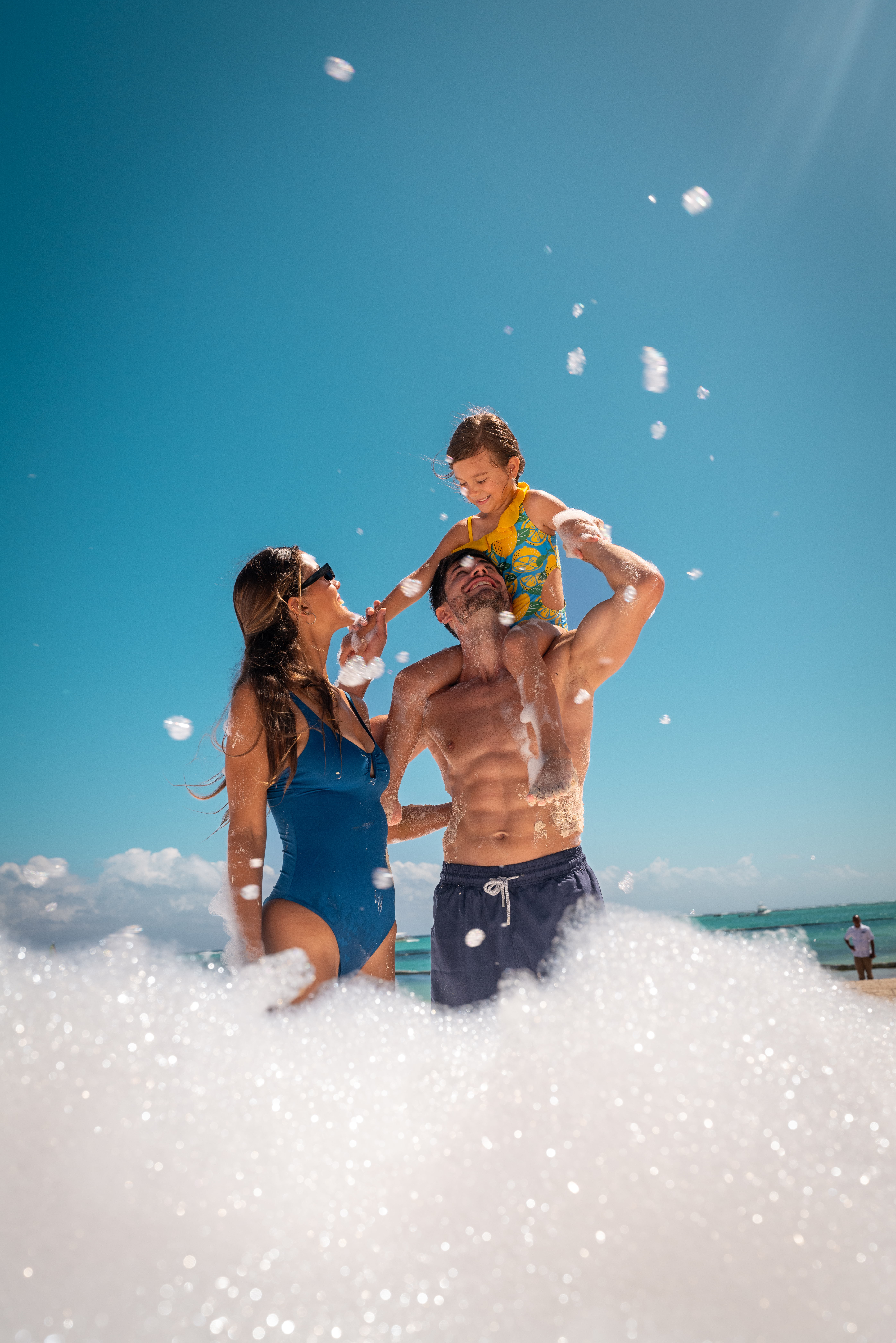 Family vacation: parents and child enjoying foam on sunny beach.