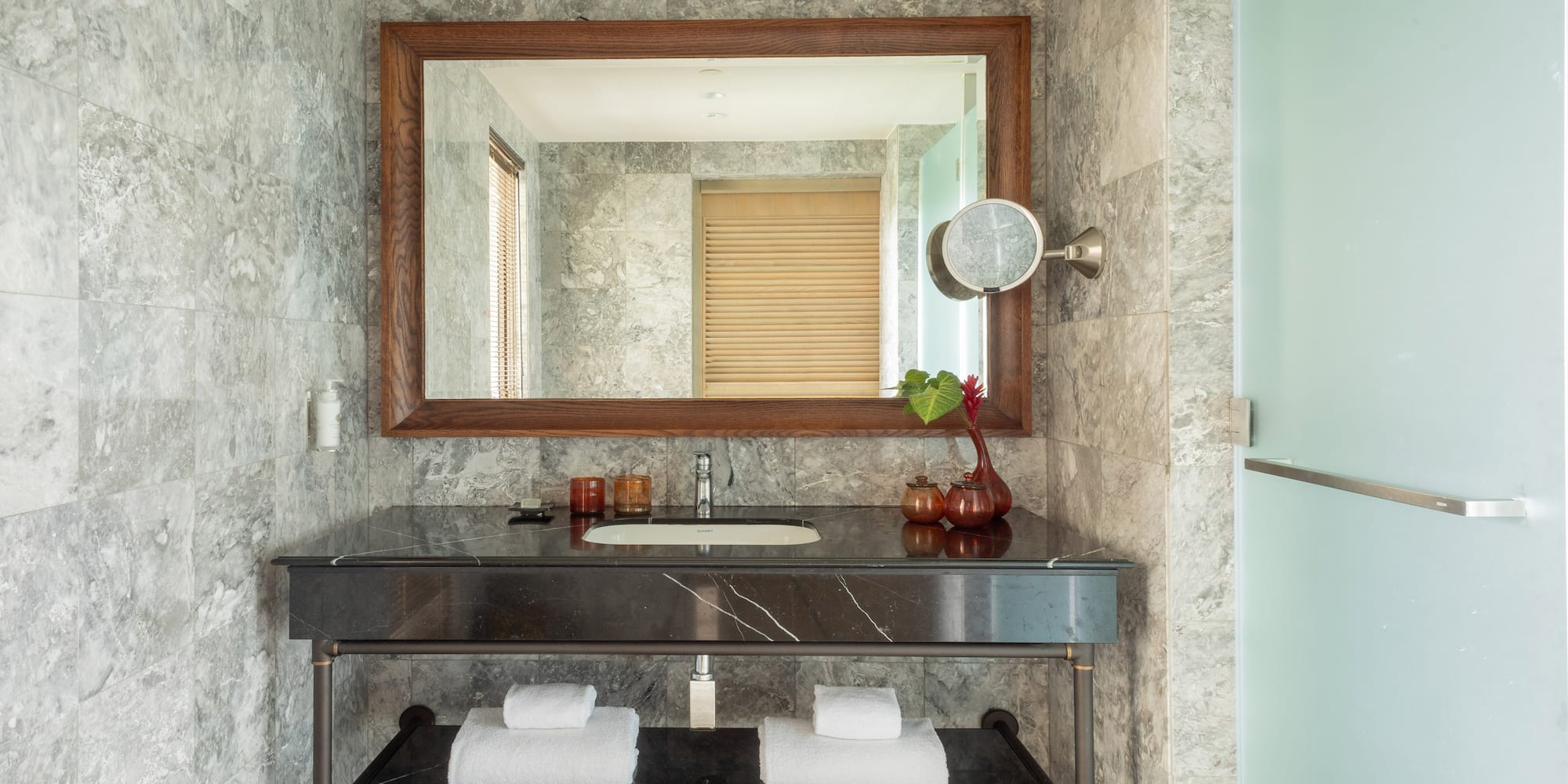 Modern bathroom vanity with gray marble walls, black countertop, and large mirror.