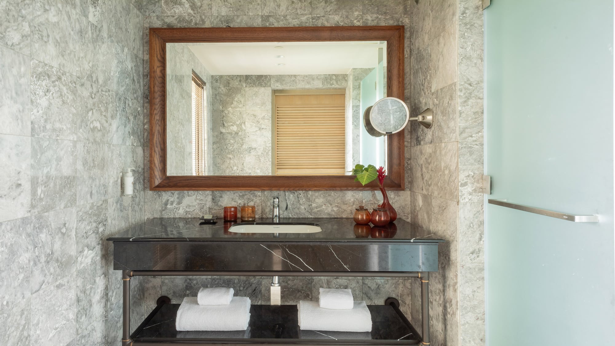Modern bathroom vanity with gray marble walls, black countertop, and large mirror.