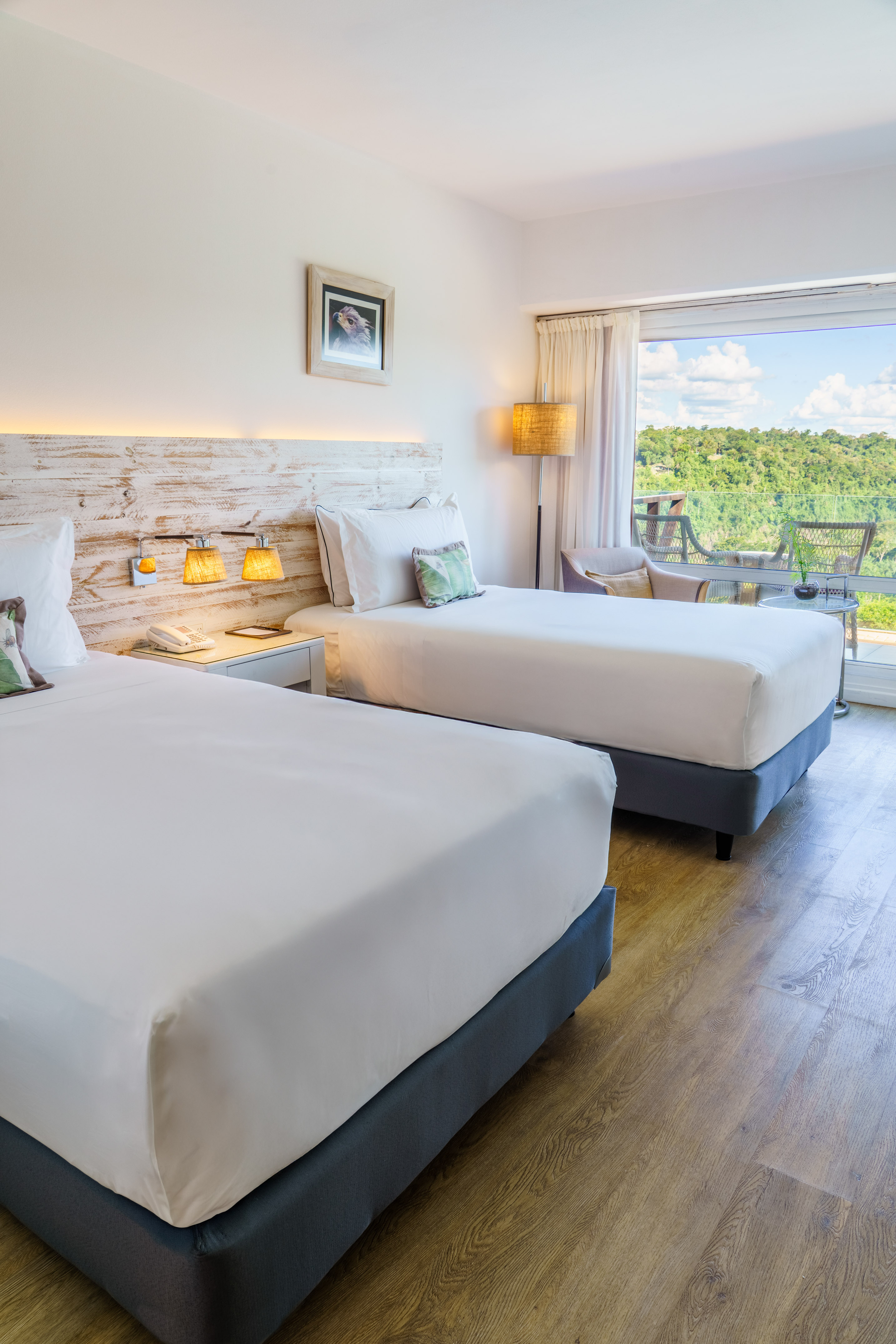 Twin hotel room with natural wood accents and a scenic forest view balcony.