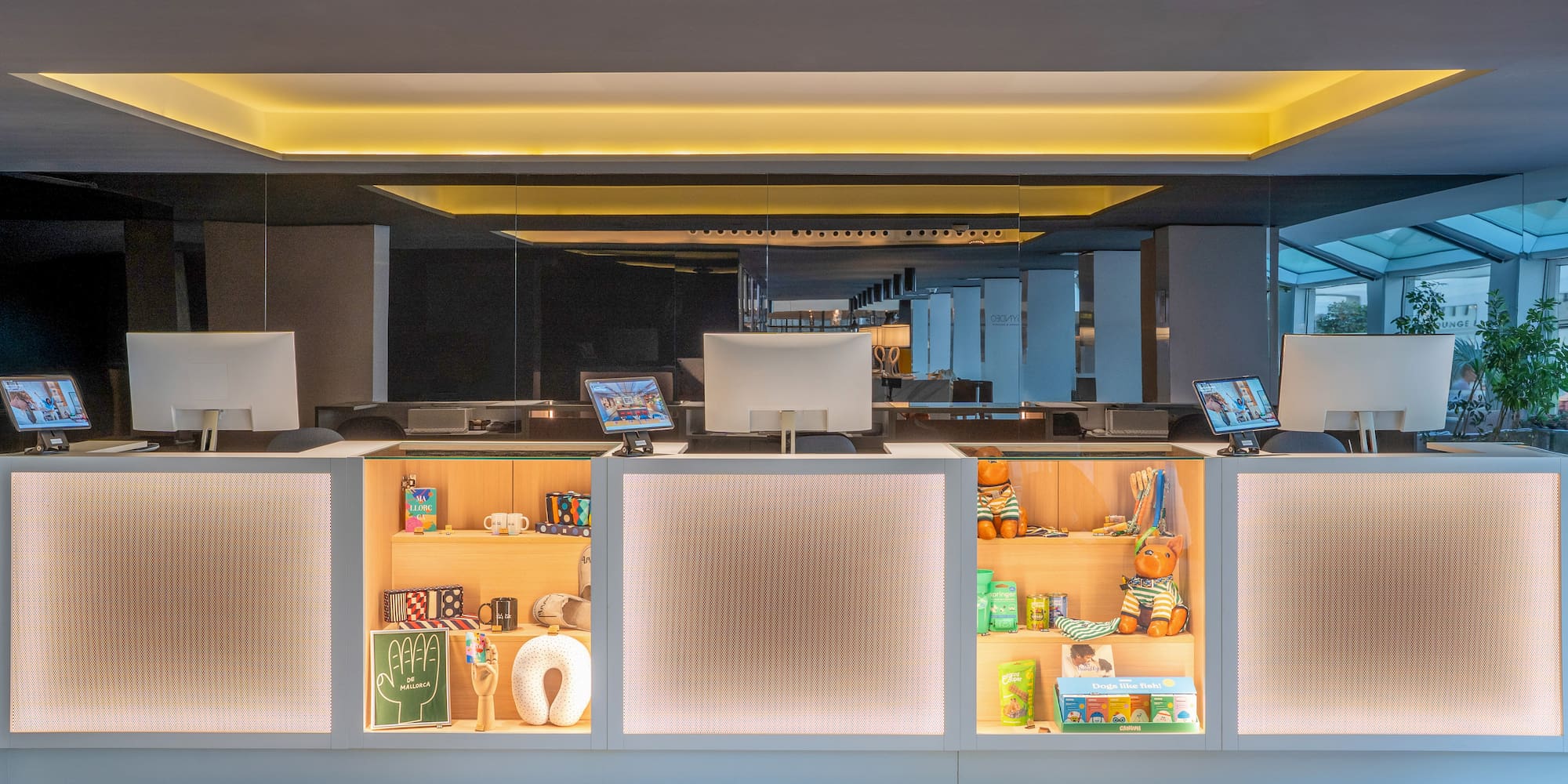 Modern hotel reception desk, computers, illuminated shelves with merchandise.