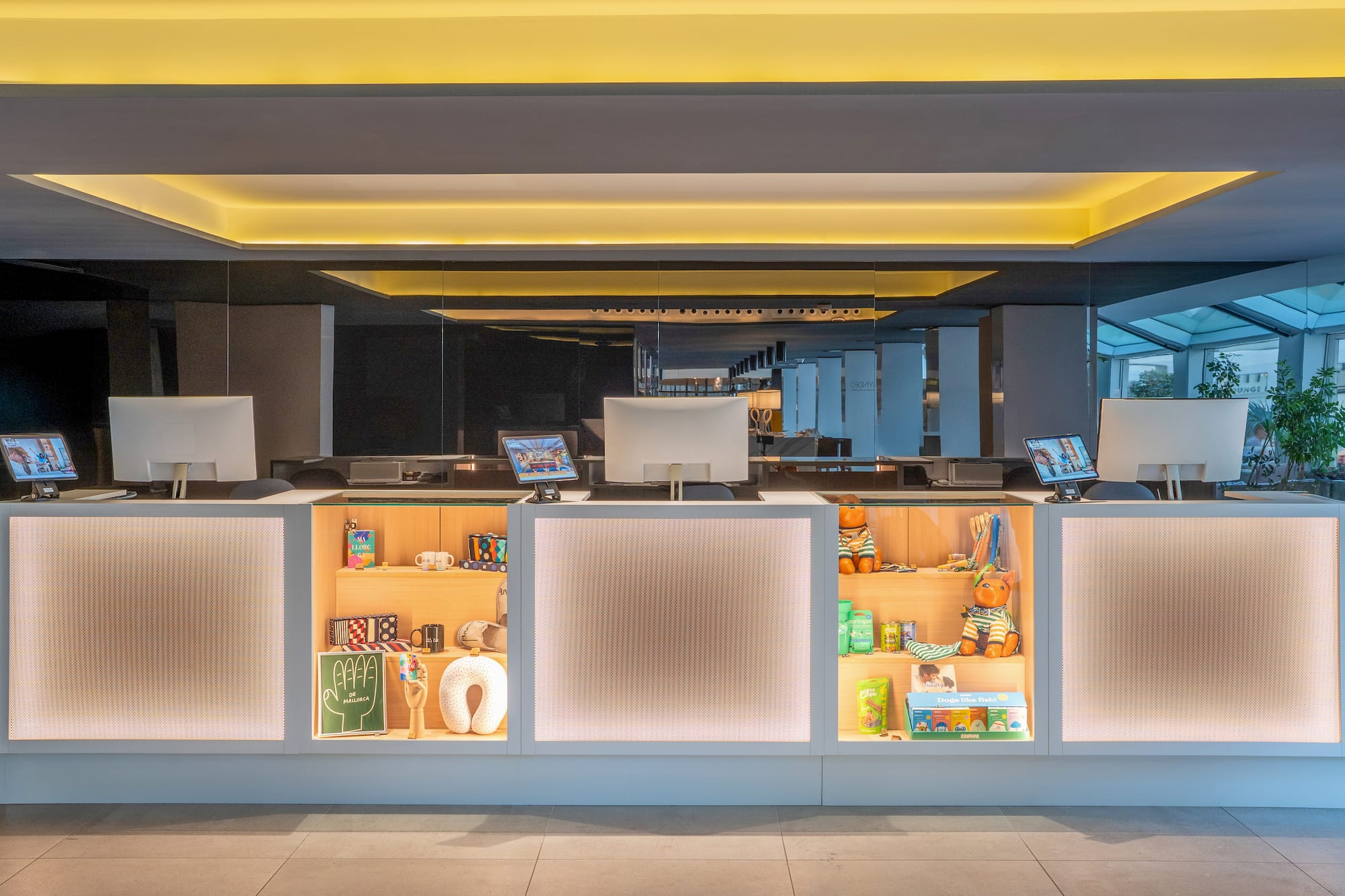 Modern hotel reception desk, computers, illuminated shelves with merchandise.