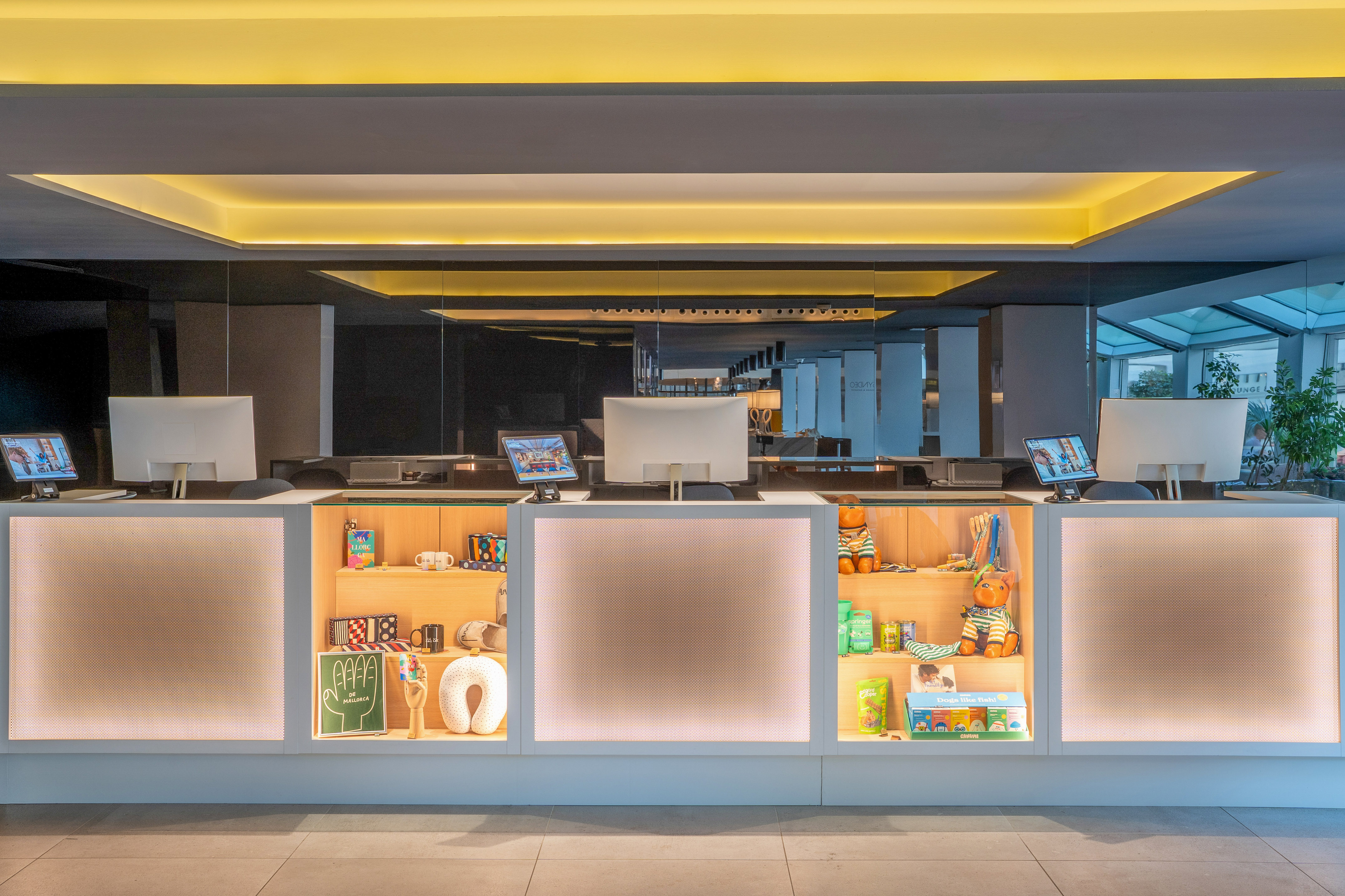 Modern hotel reception desk, computers, illuminated shelves with merchandise.
