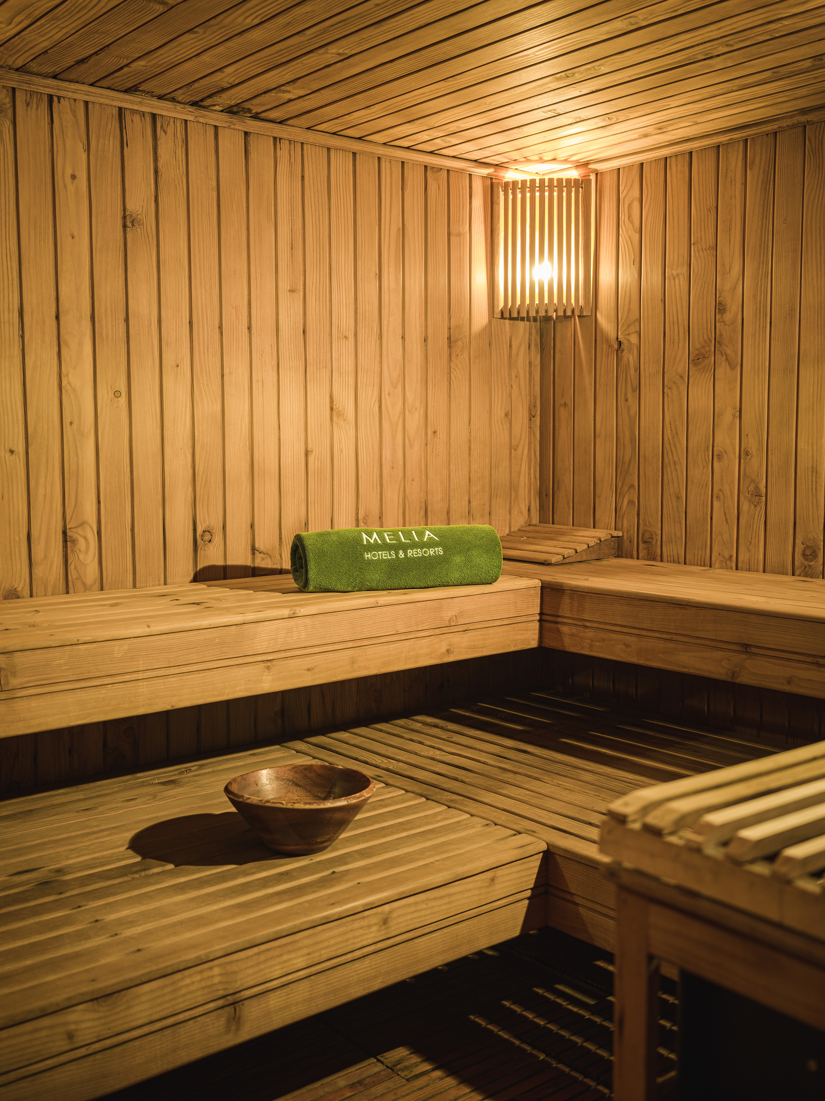 Meliá Hotels & Resorts wooden sauna with benches, warm lighting, and bowl.