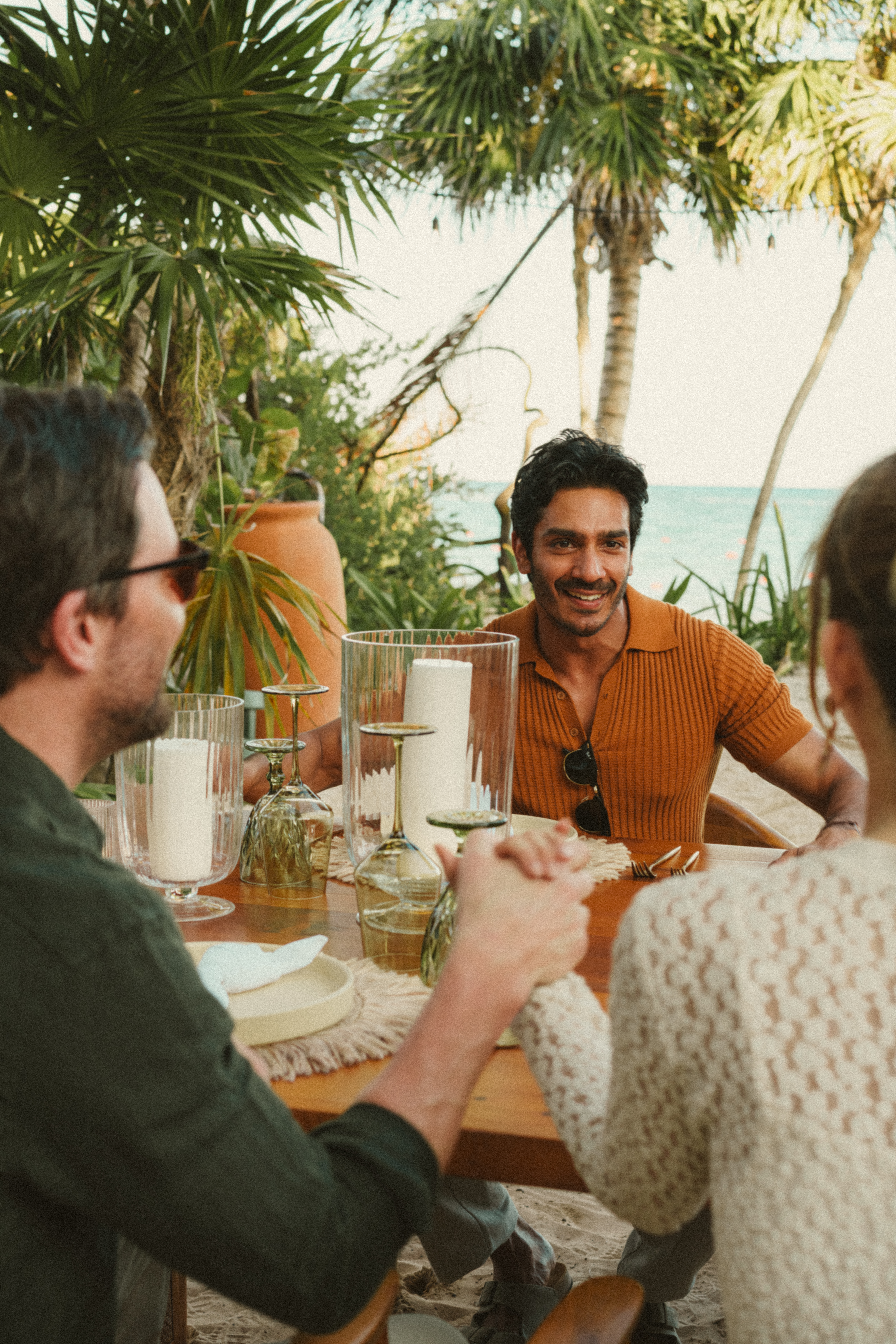 Smiling man at a tropical outdoor dinner with friends by the ocean.