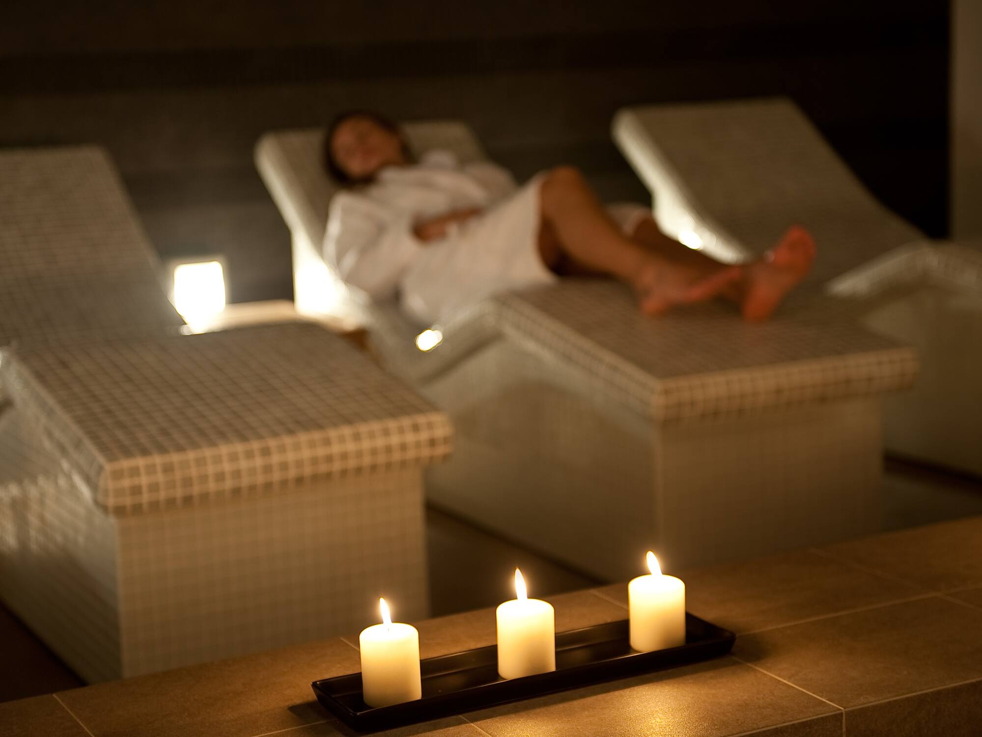 a woman lying on a lounge chair with candles in the background