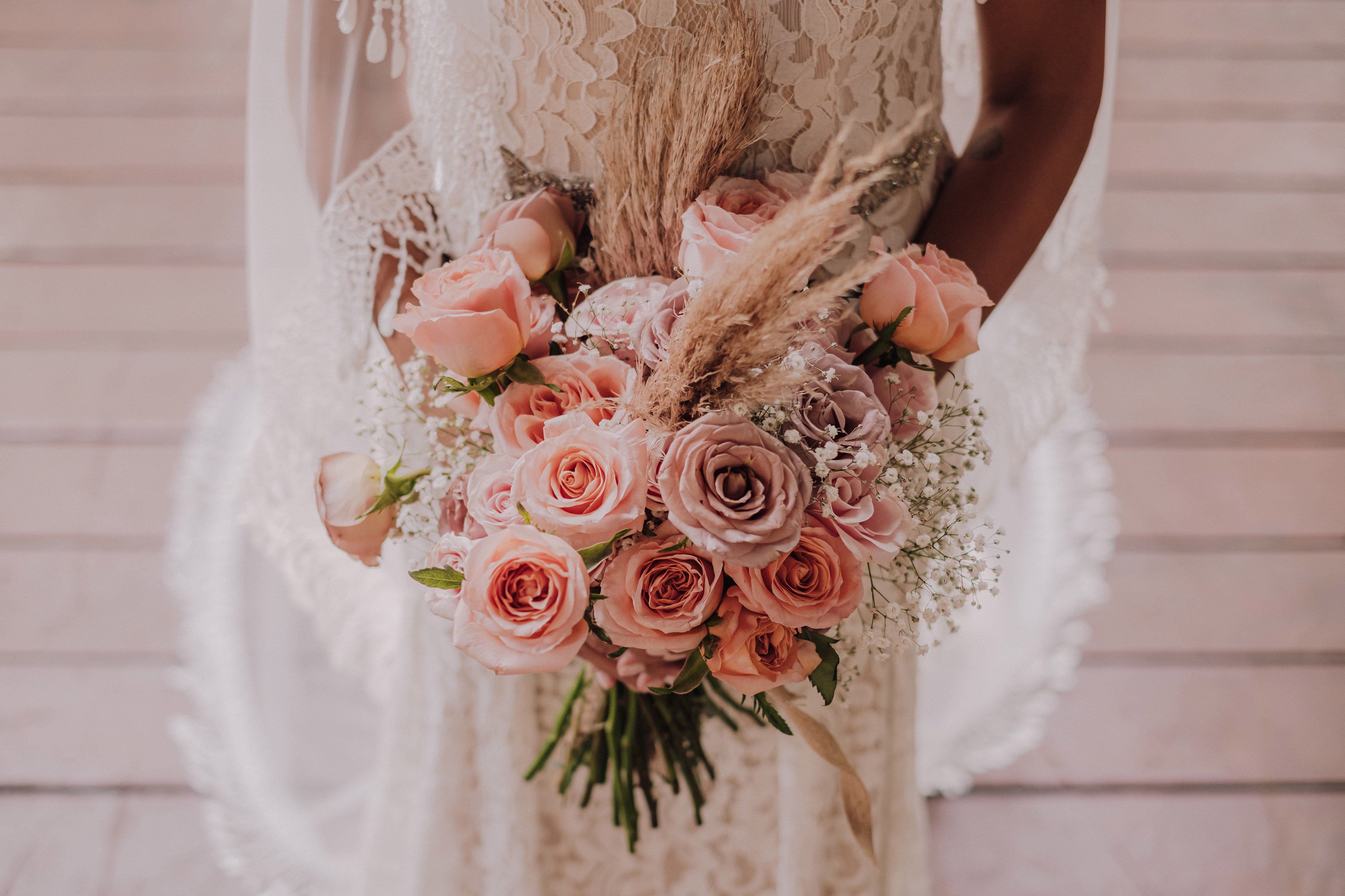 Bride holding romantic wedding bouquet with pink roses, baby's breath, and pampas grass.