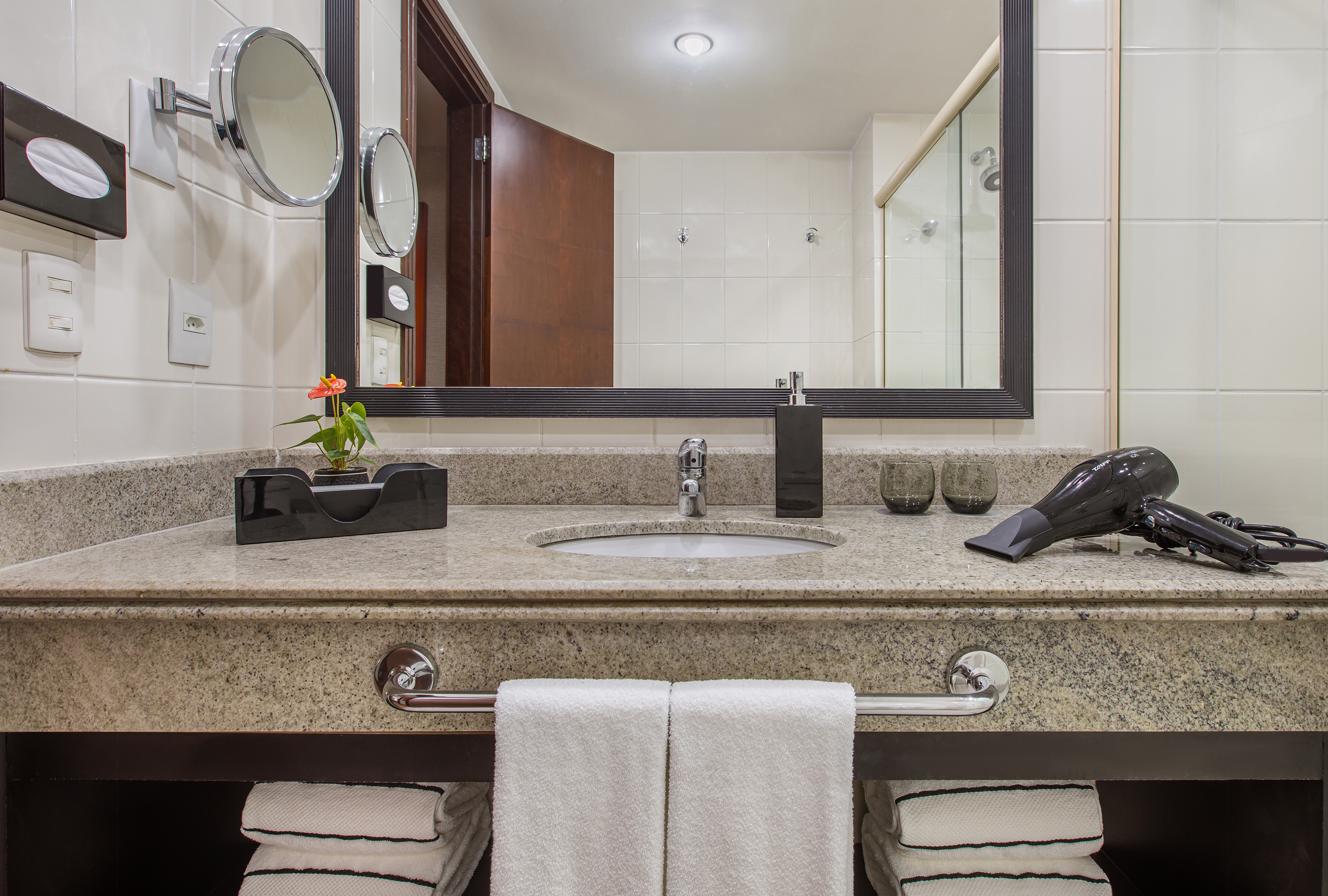 Granite bathroom vanity with sink, large mirror, hair dryer, and white towels.