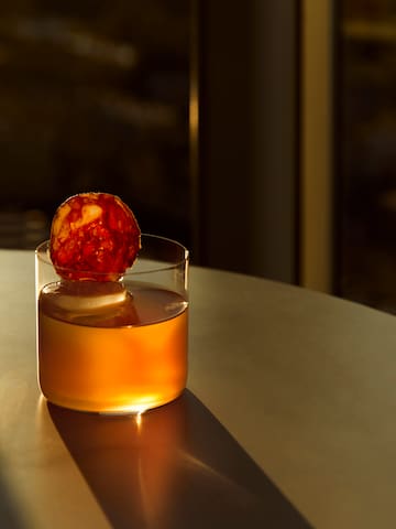 a glass of liquid with a slice of sausage on top